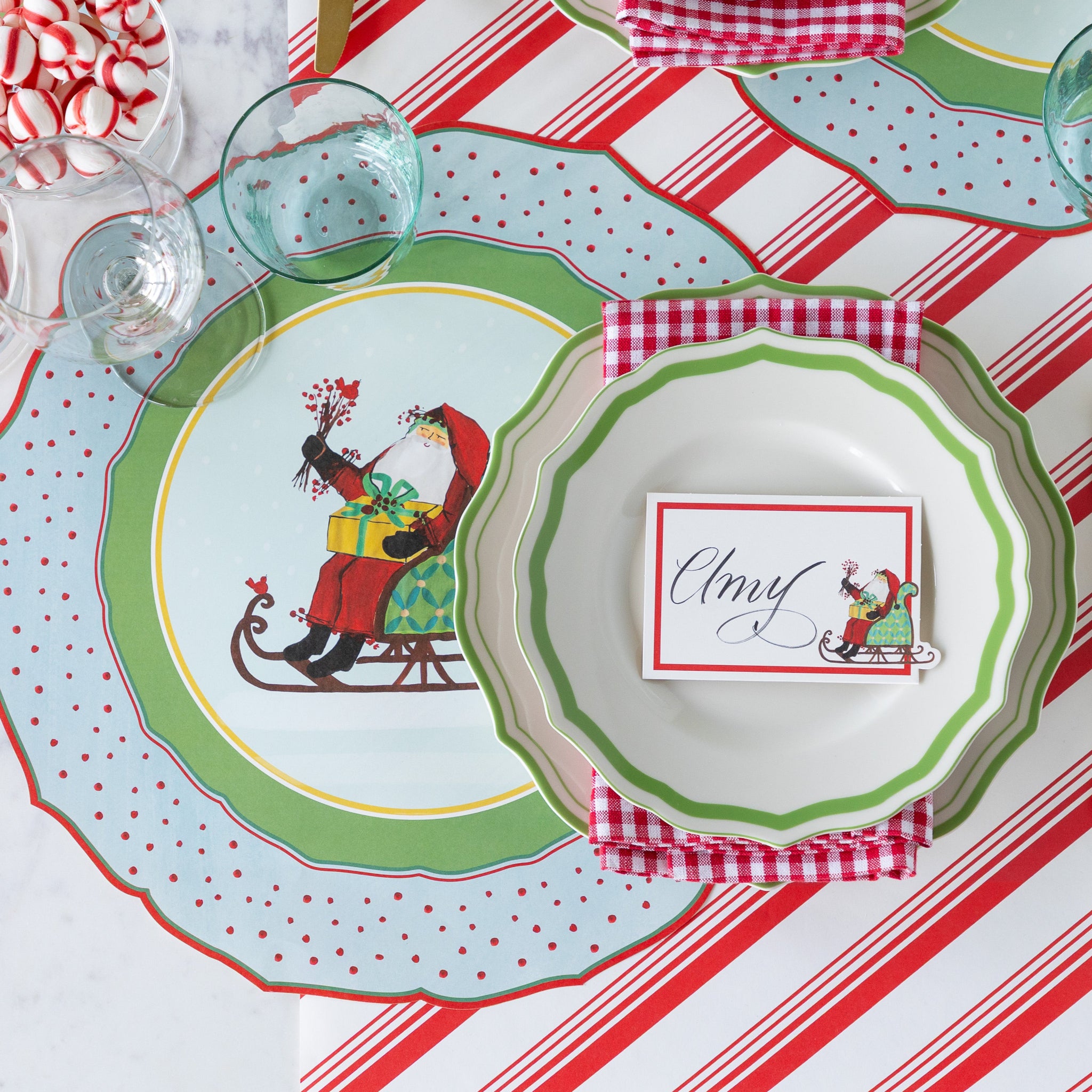 Christmas-themed table setting with Green Icing on the Cake plates, red-and-white checkered napkins and Die-cut Old St. Nick Sleigh Placemat on the Peppermint Stripe Runner.