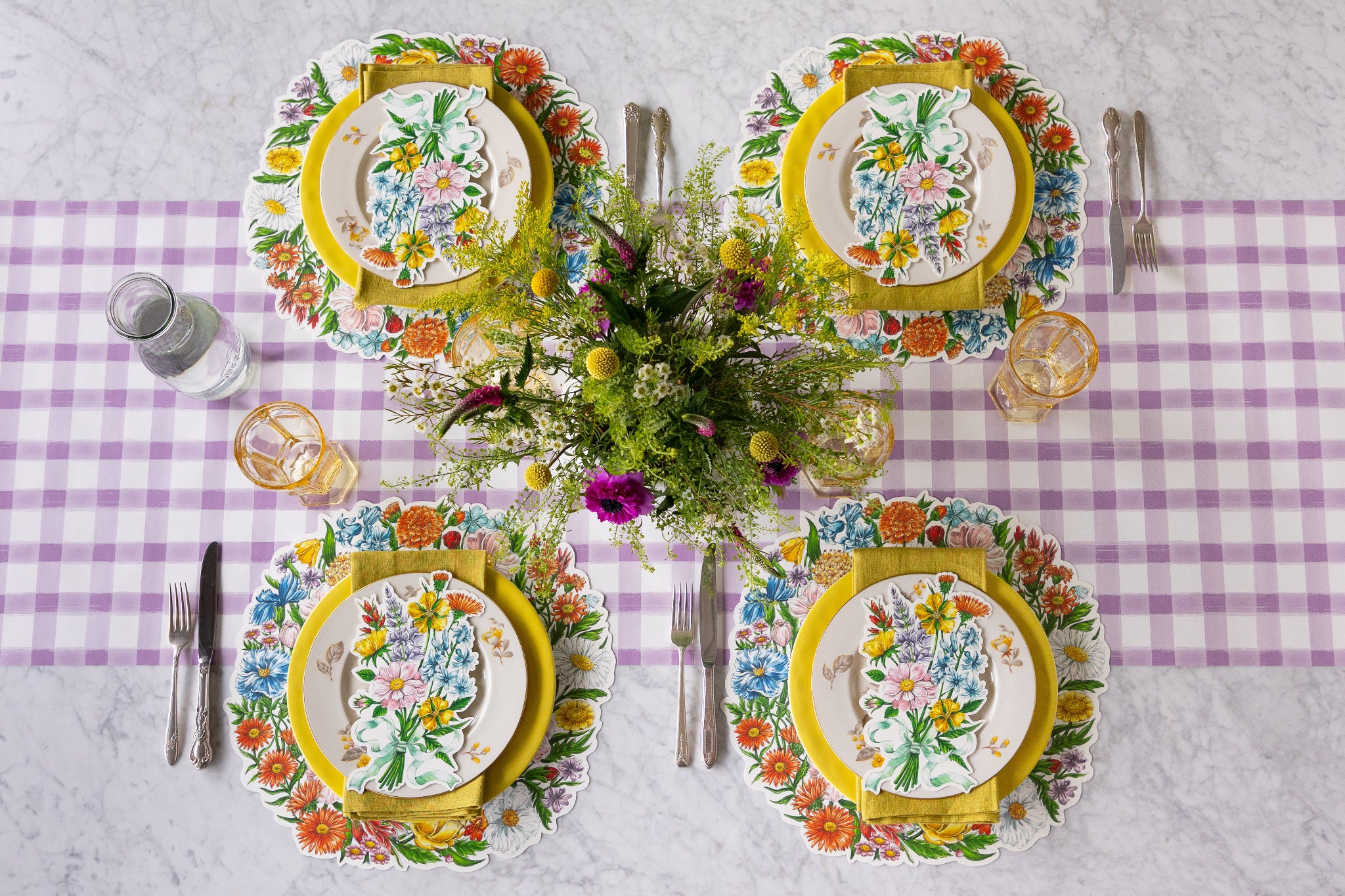 Table setting with a floral arrangement, Die-cut Wildflower Wreath Placemats, Wildflower Table Accents and colorful plates on the Lilac Painted Check Runner.