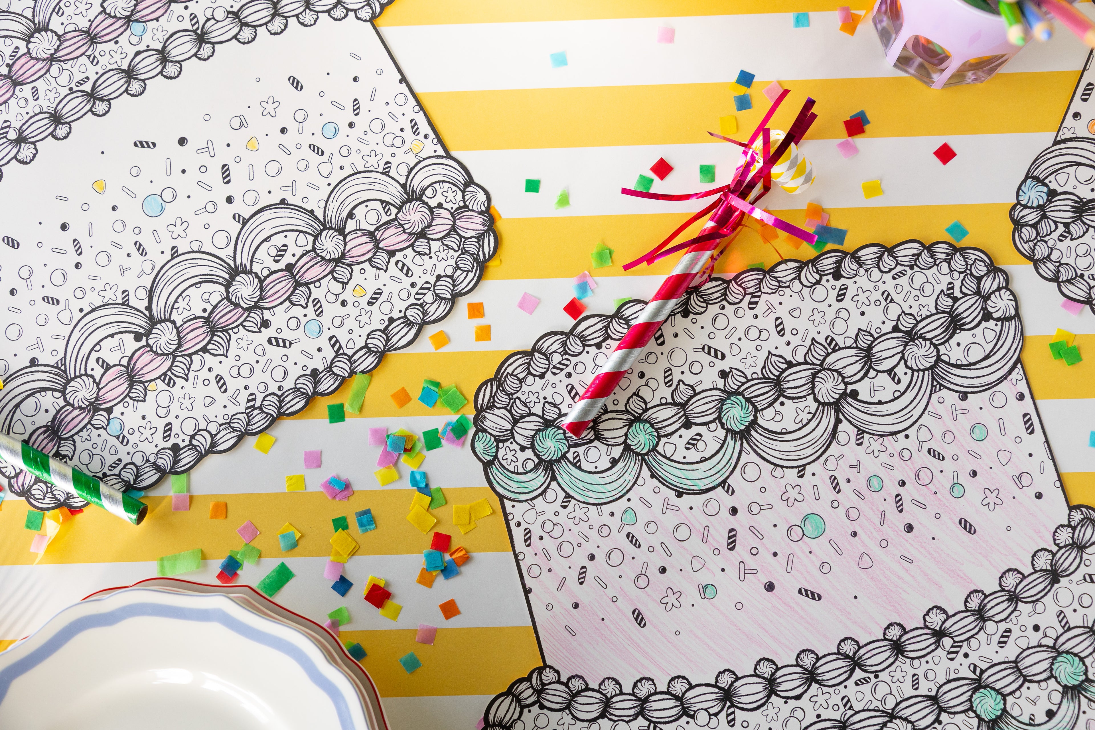 Die-cut Coloring Birthday Cake Placemats partially colored in on a table with confetti.