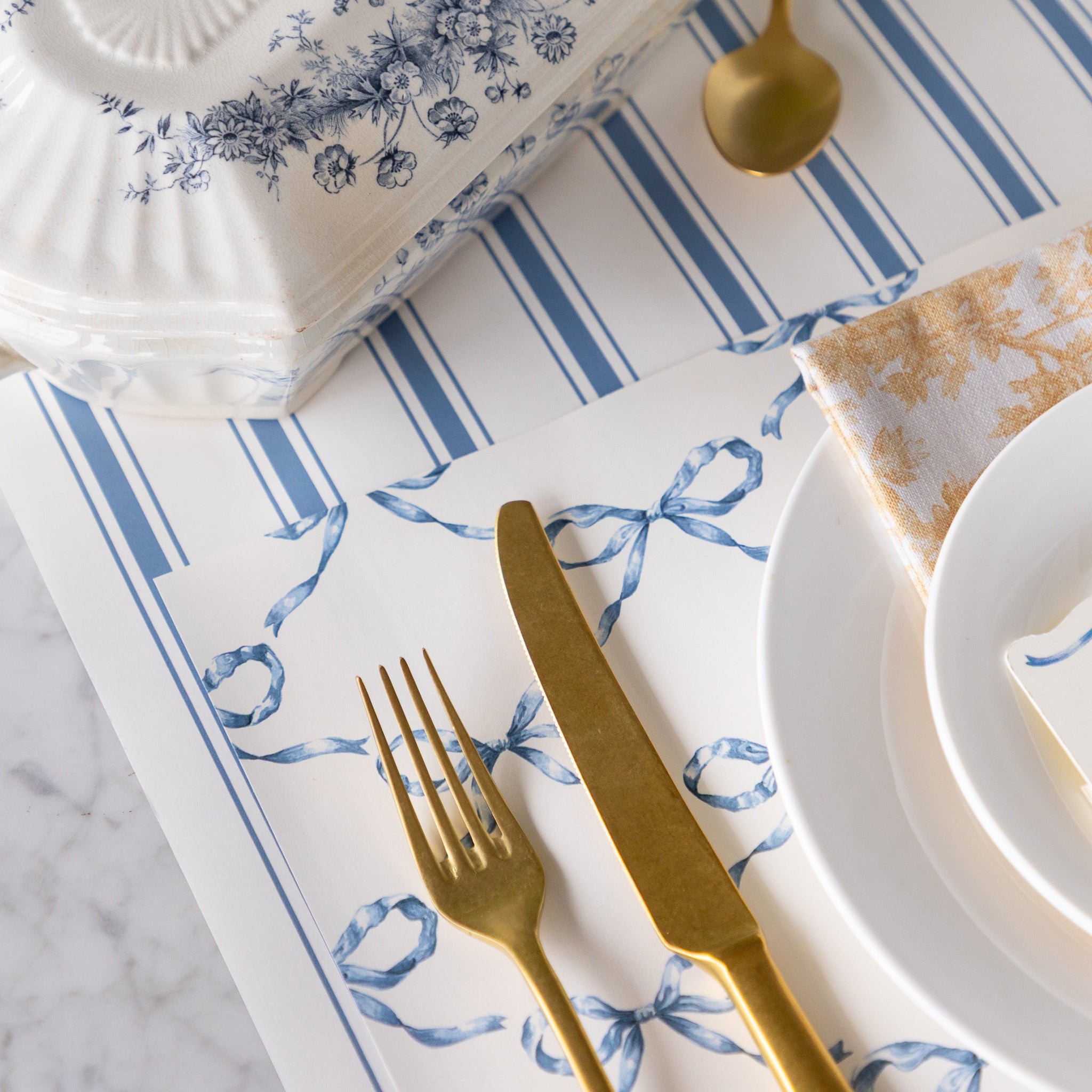 Close up of the Heirloom Blue Bow Lattice Placemat under a place setting with the Cornflower Blue Linen Stripe Runner underneath.