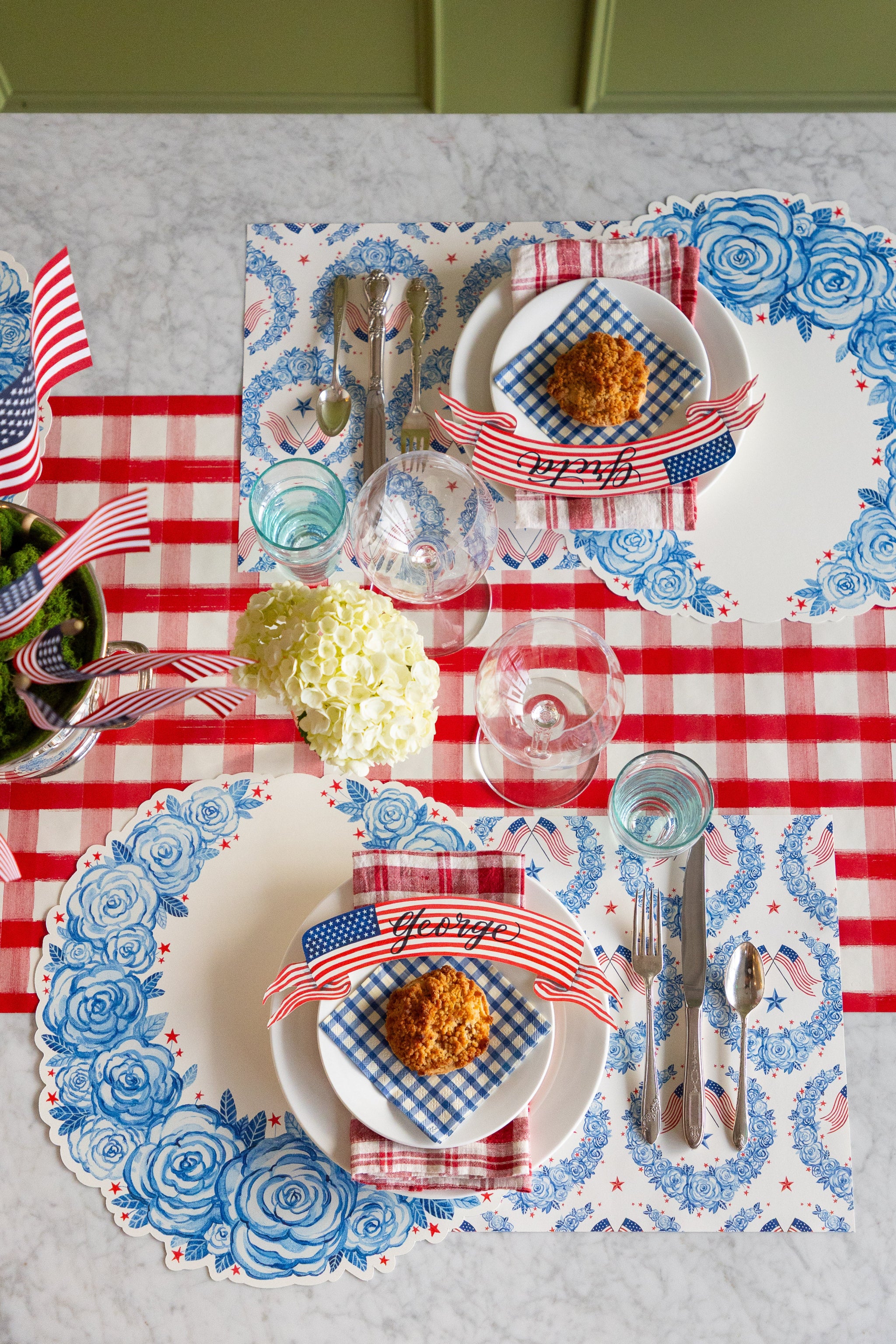 Dining table set with Die-cut American Floral Wreath Placemats, American Floral Placemats, American Flag Banner Table Accents and red-and-white decorative elements on the Red Painted Check Runner.