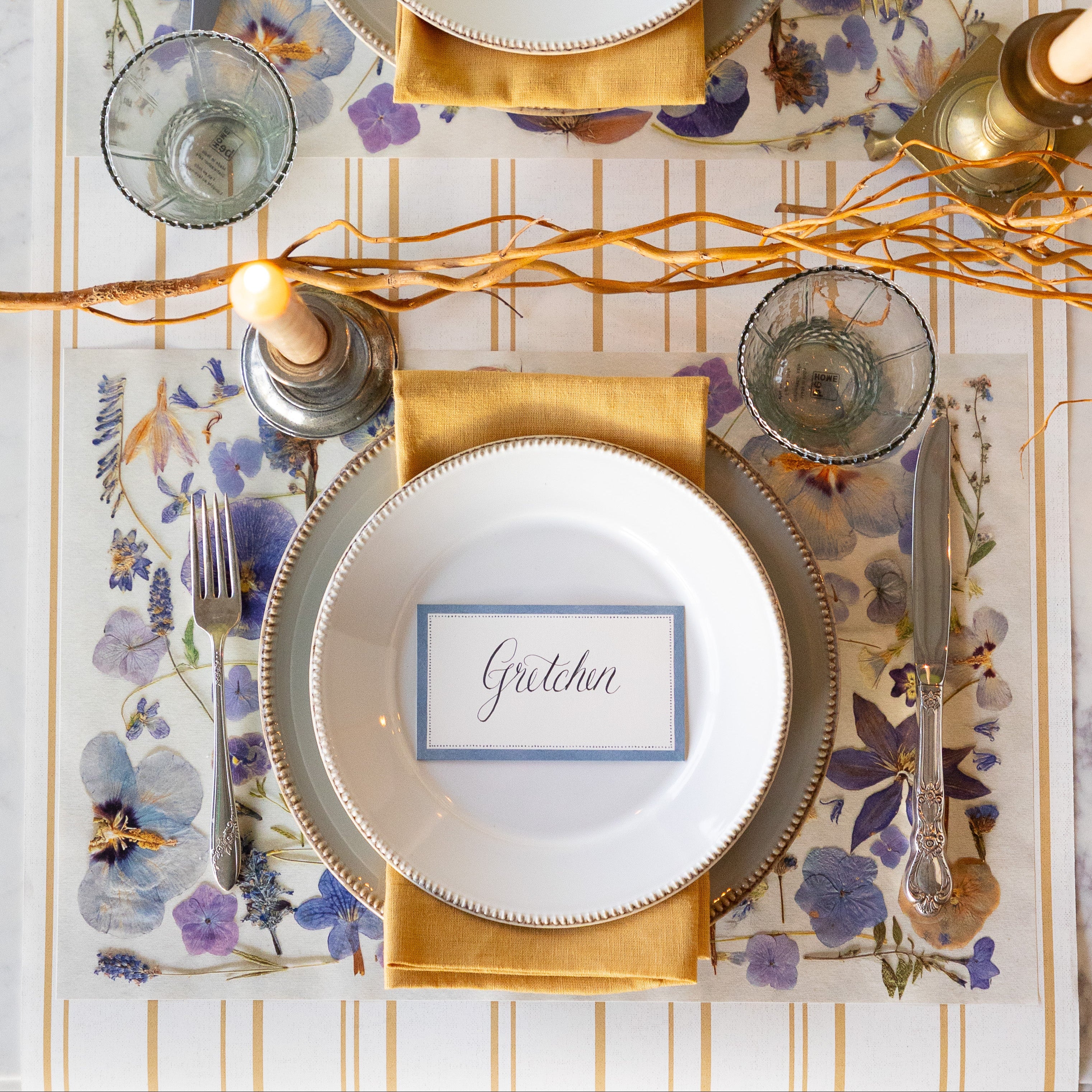 Elegant table setting with Periwinkle Pressed Petals Placemat, decorative plates, Cornflower Blue Place Card and decorative elements on the Antique Gold Stripe Runner.