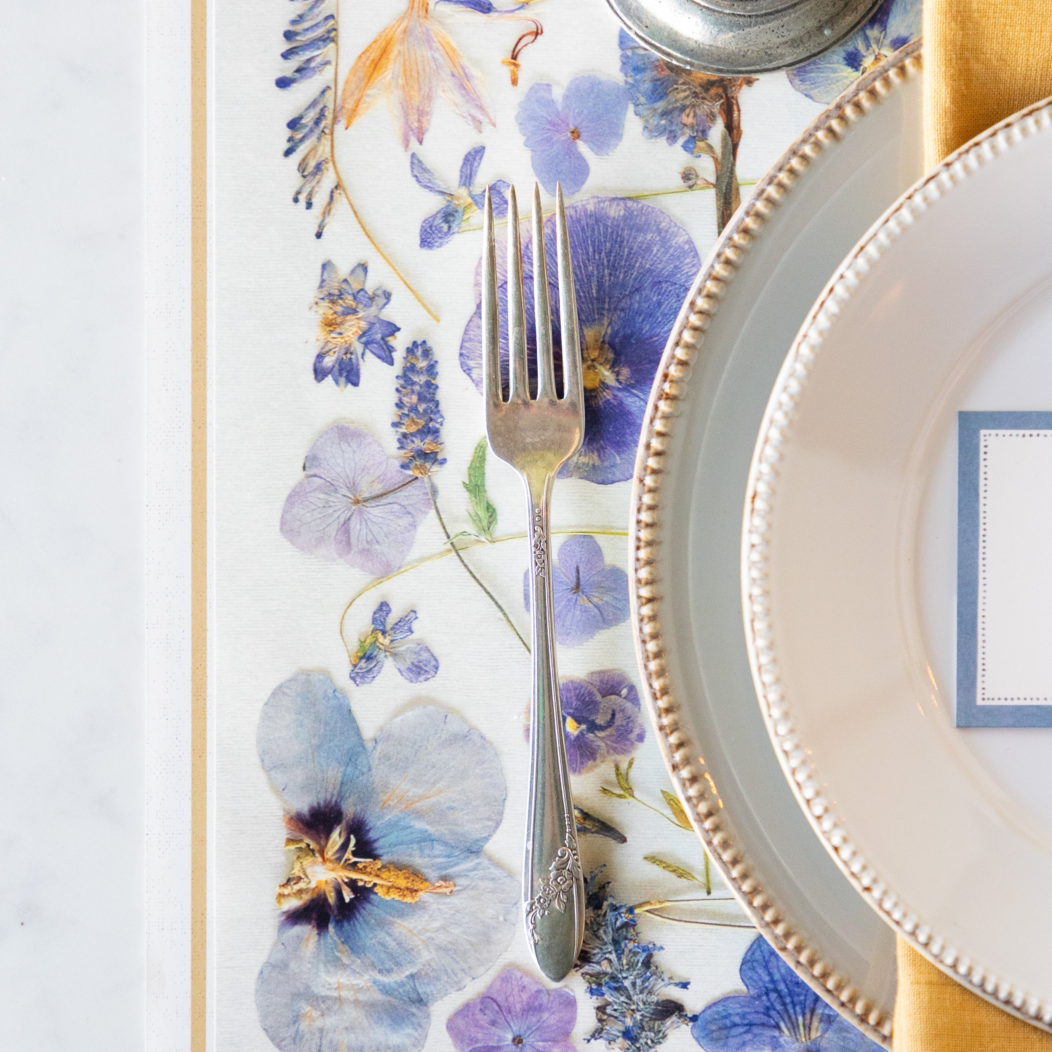 Decorative table setting with floral placemat, silverware, and plates.