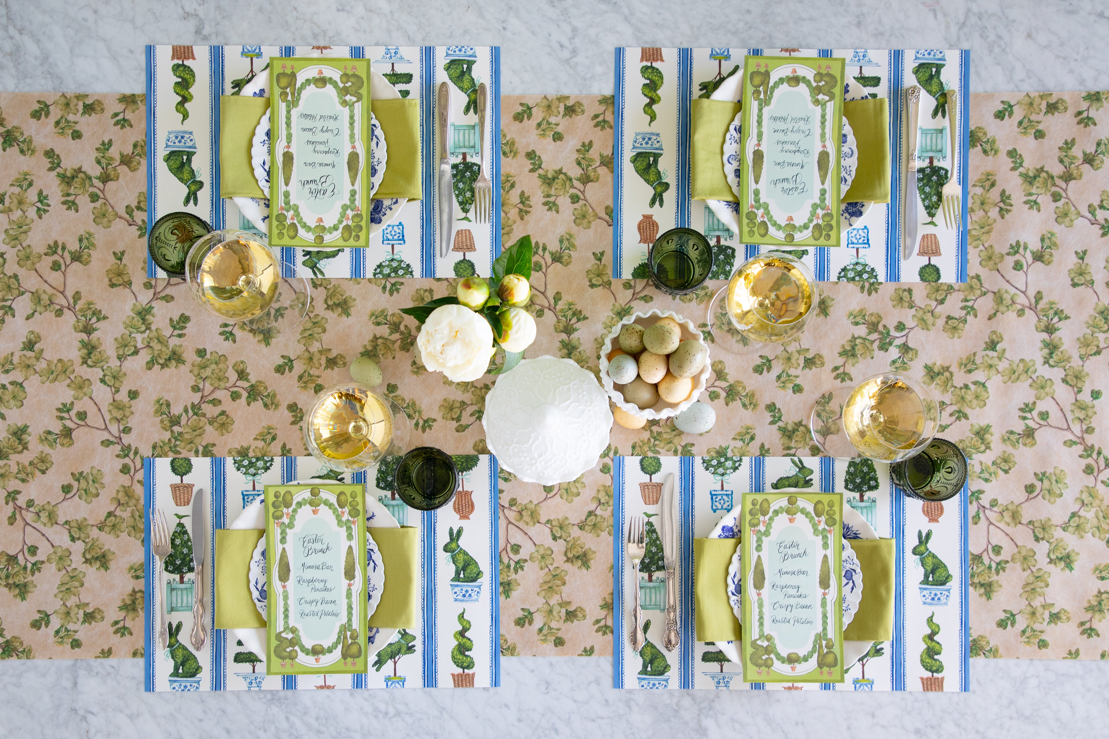 Easter table setting with eggs, flowers, Spring Topiary Placemats, Topiary Garden Table Cards, floral plates and greens napkin on the Green Cherry Blossom Runner.
