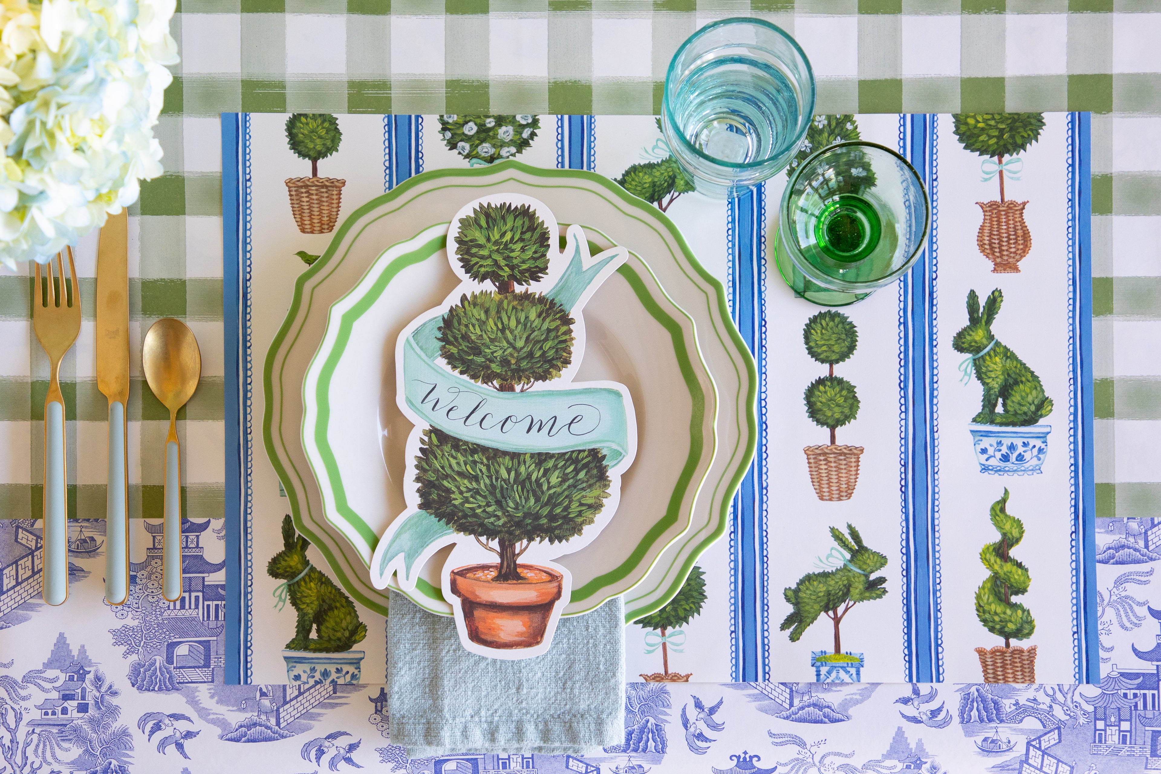 Place setting with the Spring Topiary Placemat, Topiary Table Accent, Green Icing on the Cake Plates, seafoam napkin and cutlery on the Moss Painted Check and Blue Regal Peacock Runners.