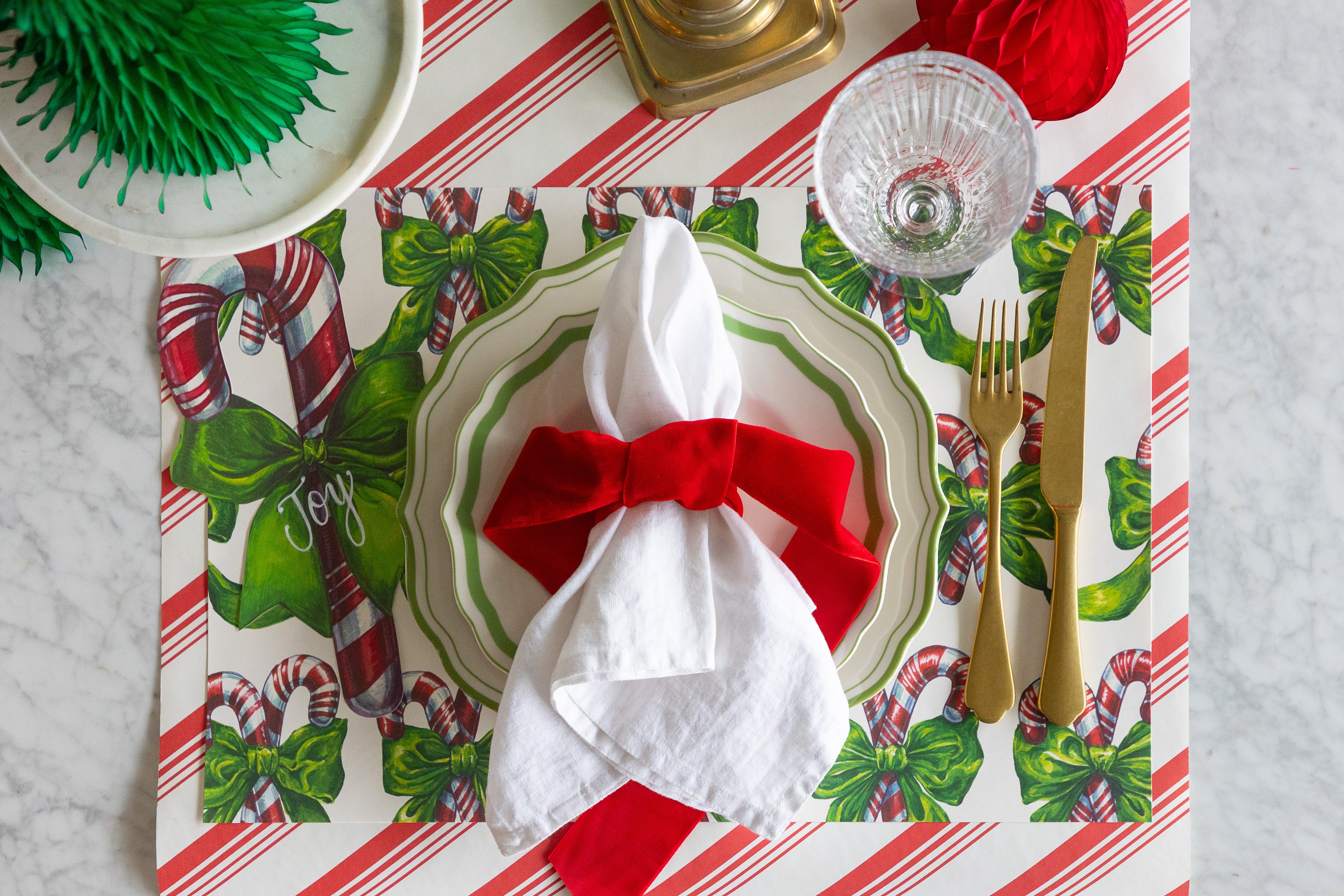 Christmas-themed table setting with a red napkin, gold cutlery, and festive placemat.