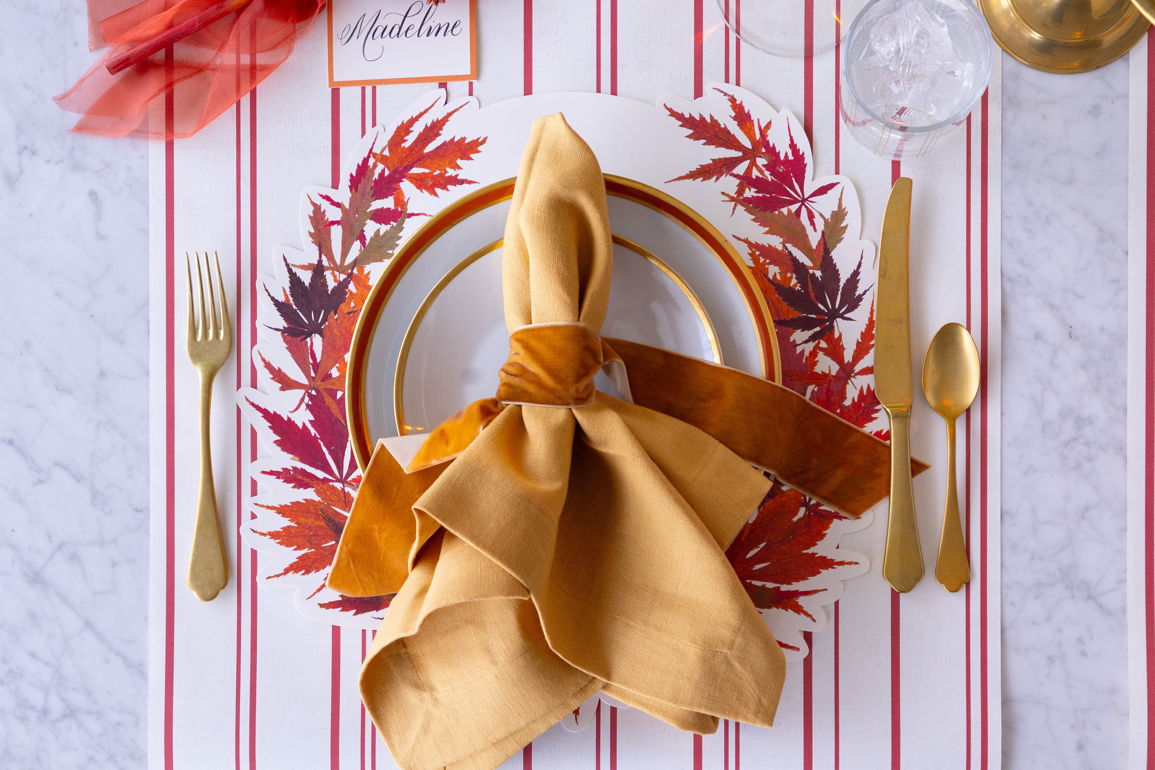 Thanksgiving table setting with gold napkin, plates, and cutlery on the Die-cut Japanese Maple Wreath Placemat.