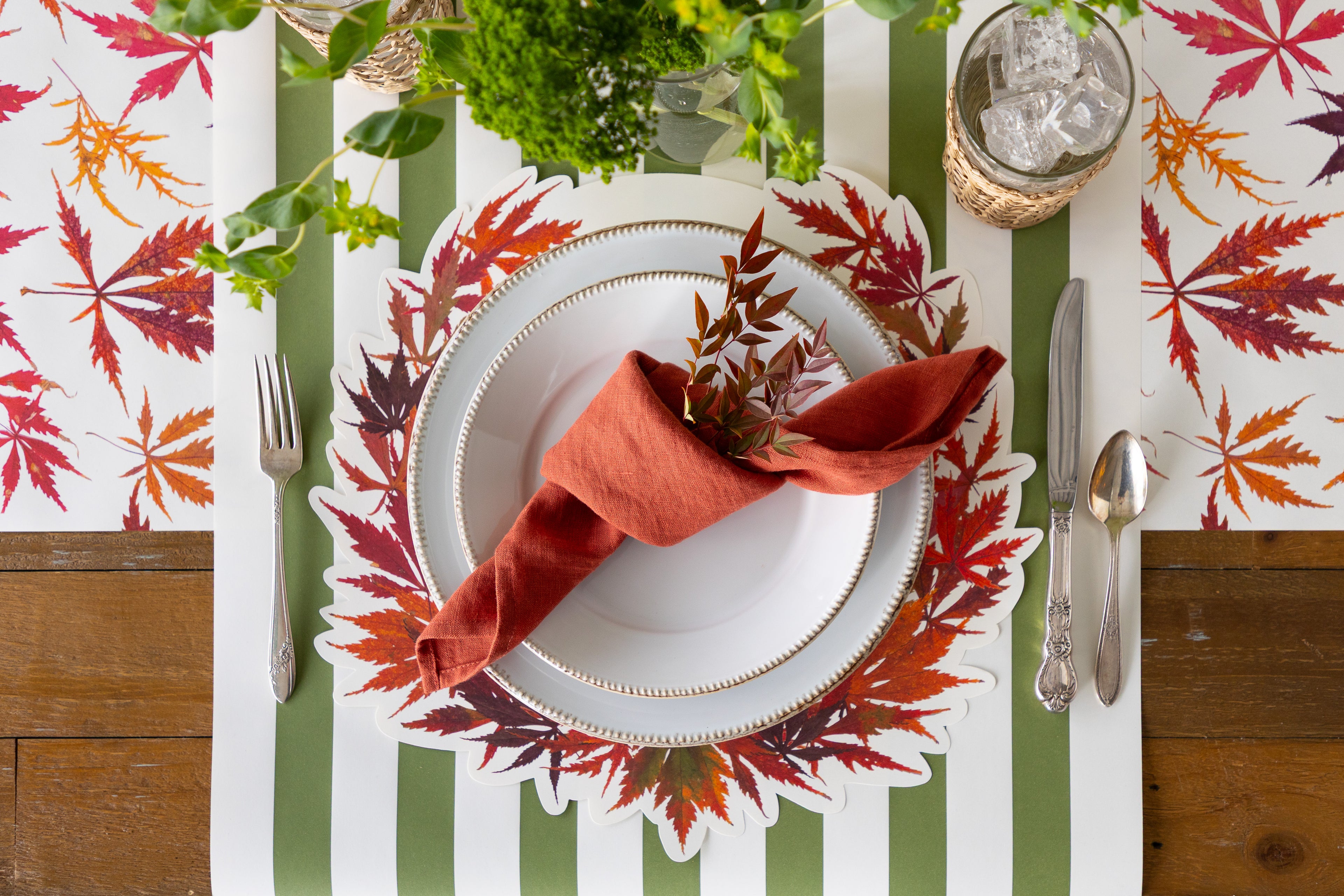 Fall table setting with napkin, plate, and cutlery on the Die-cut Japanese Maple Wreath Placemat on a green stripe runner.