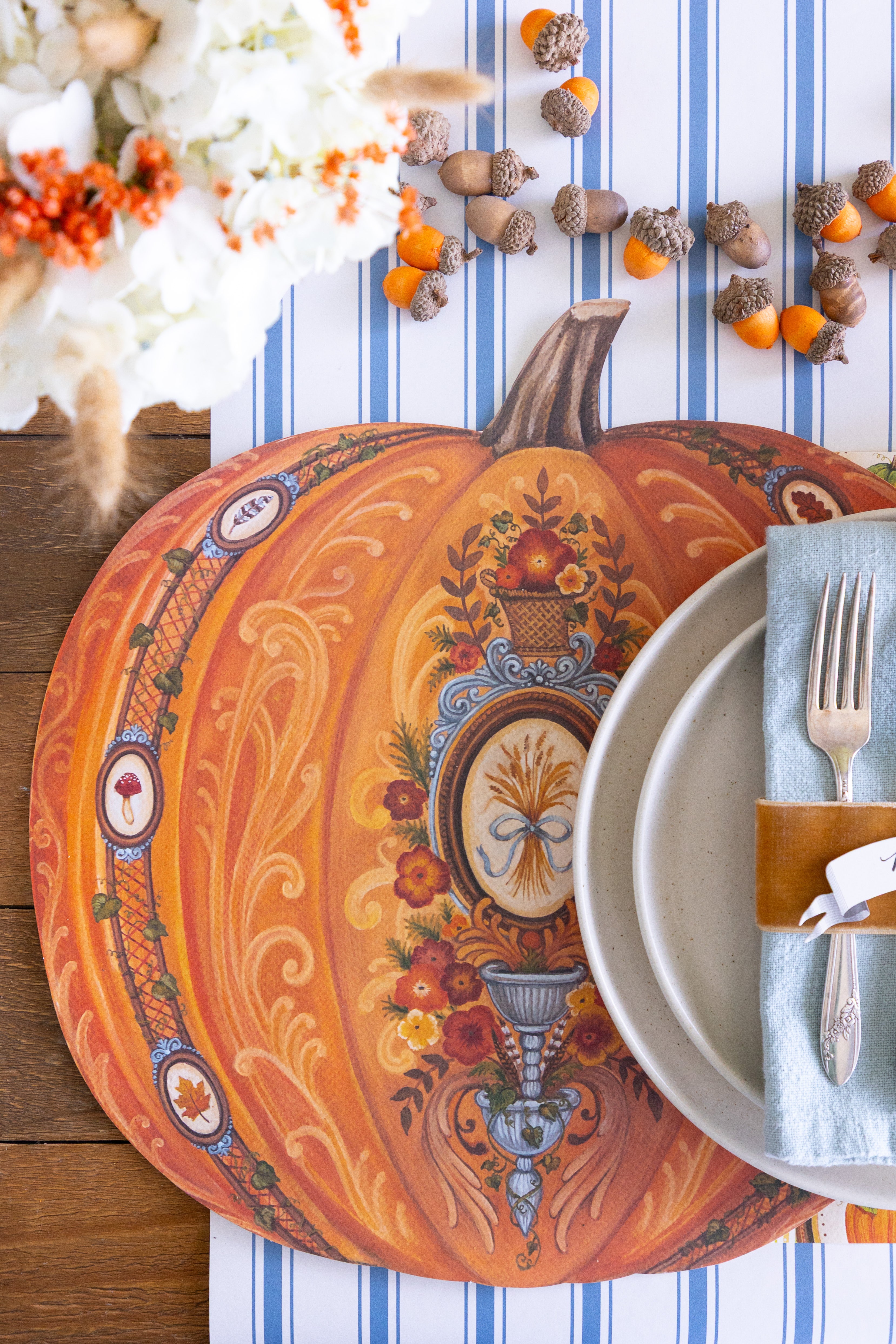 Decorative pumpkin-shaped placemat with intricate designs on a table setting with a blue and white striped table runner.