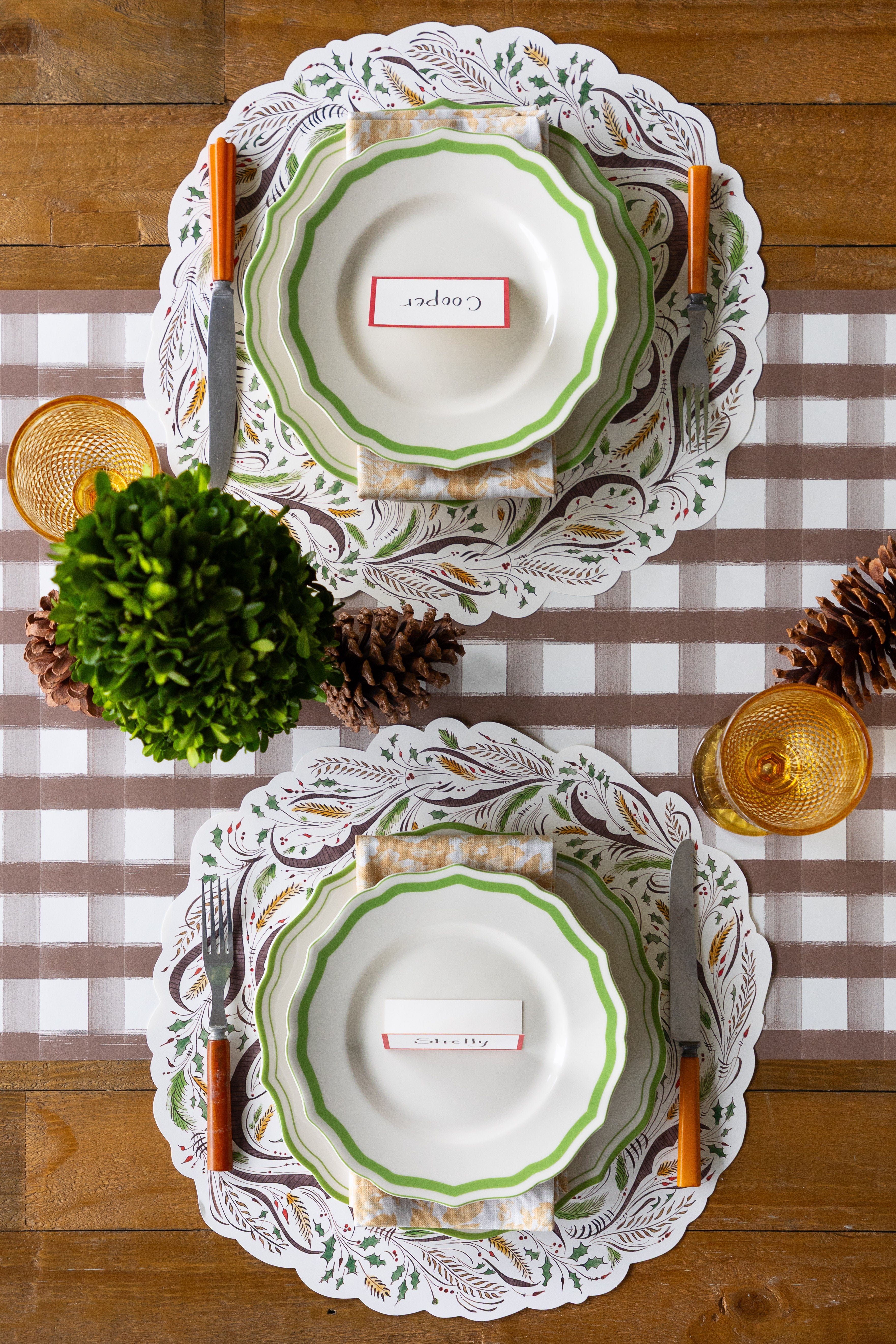 Set of plates with decorative edges on a checkered tablecloth with pinecones and greenery.