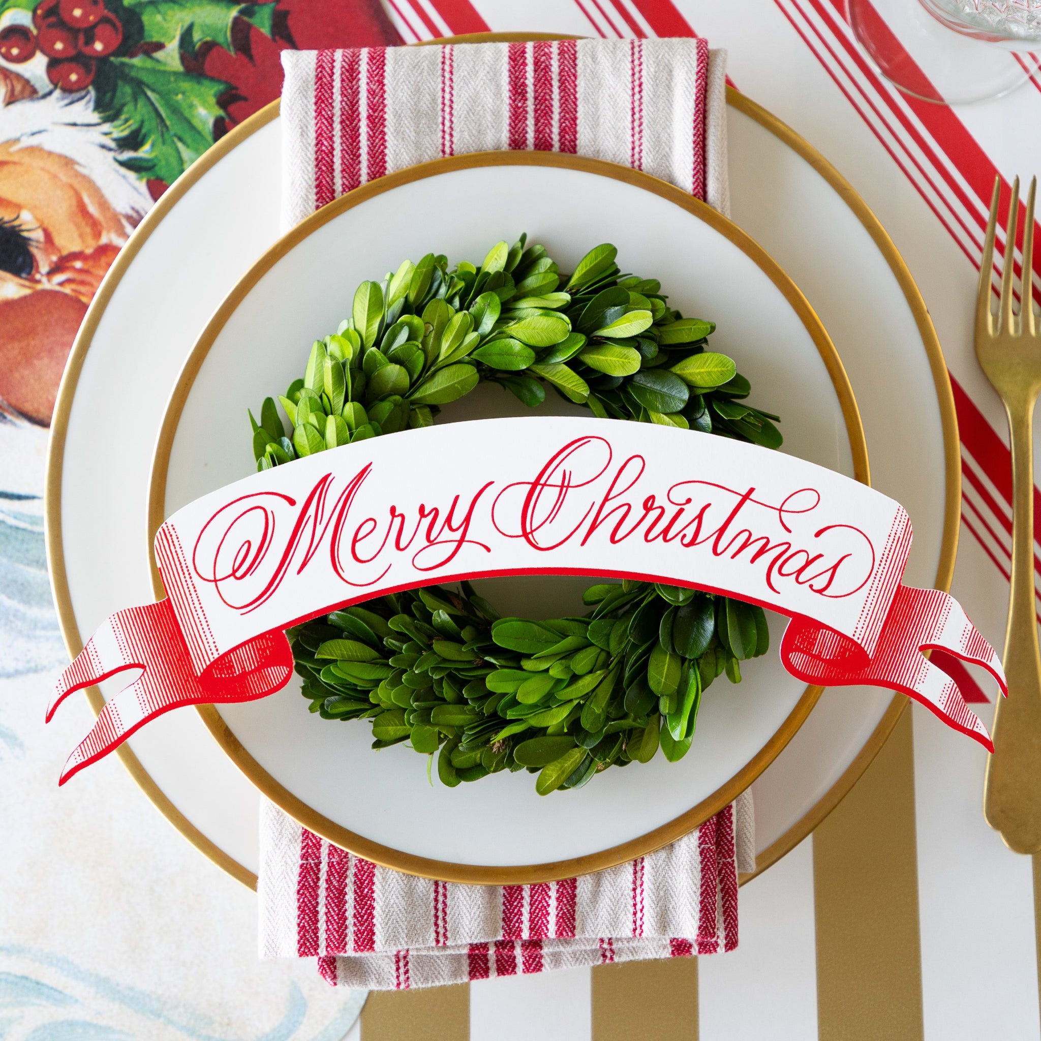 Christmas-themed place setting with a topiary wreath and Merry Christmas Table Banner Table Accent on a white plate.