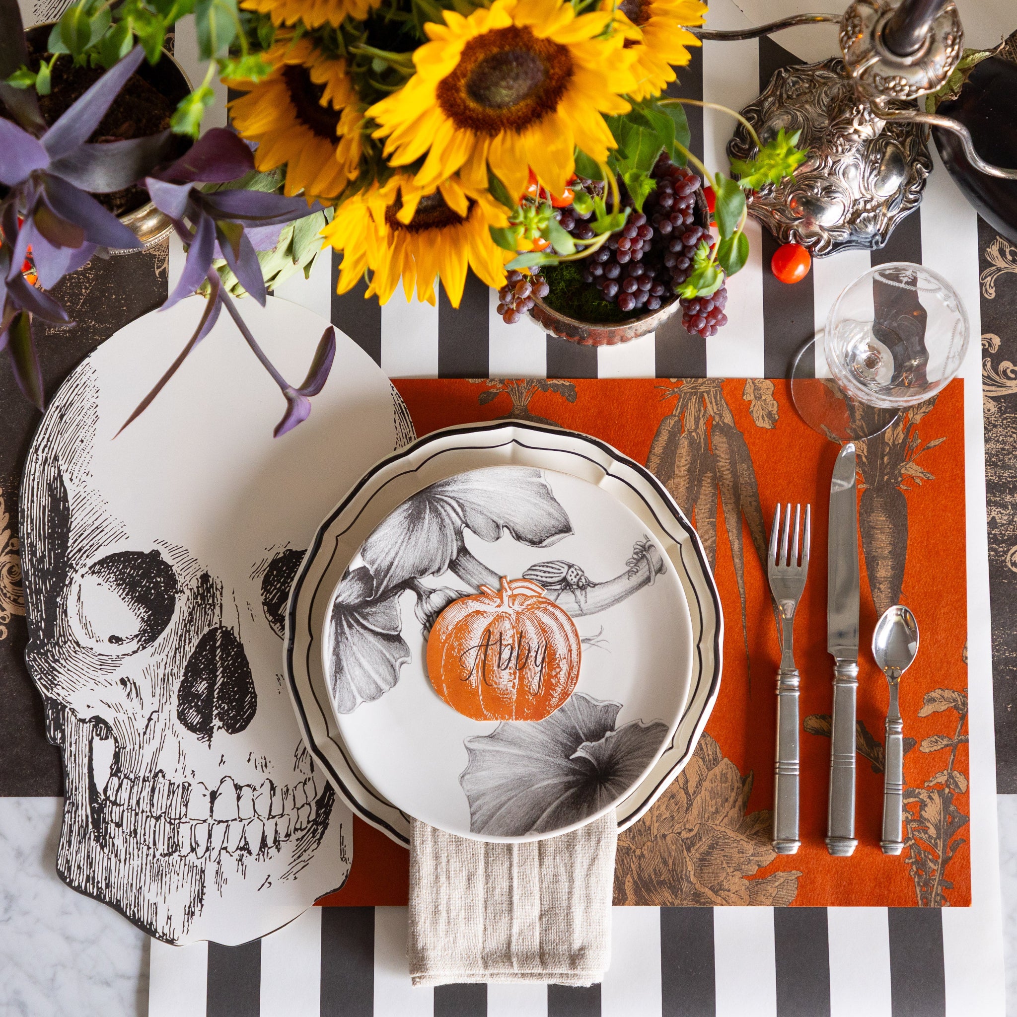 Halloween-themed table setting with the Die-cut Skull Placemat, Pumpkin Place Card and Harvest Vegetable Persimmon Placemat on the Black Classic Stripe and Archival Black Runner.