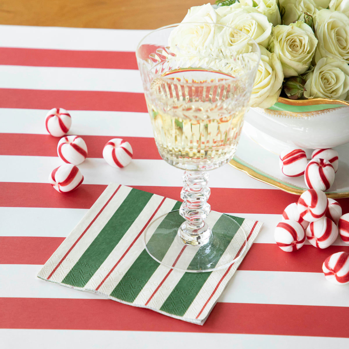 A Green &amp; Red Awning Stripe Cocktail Napkin under a champagne glass under a festive holiday tablescape.