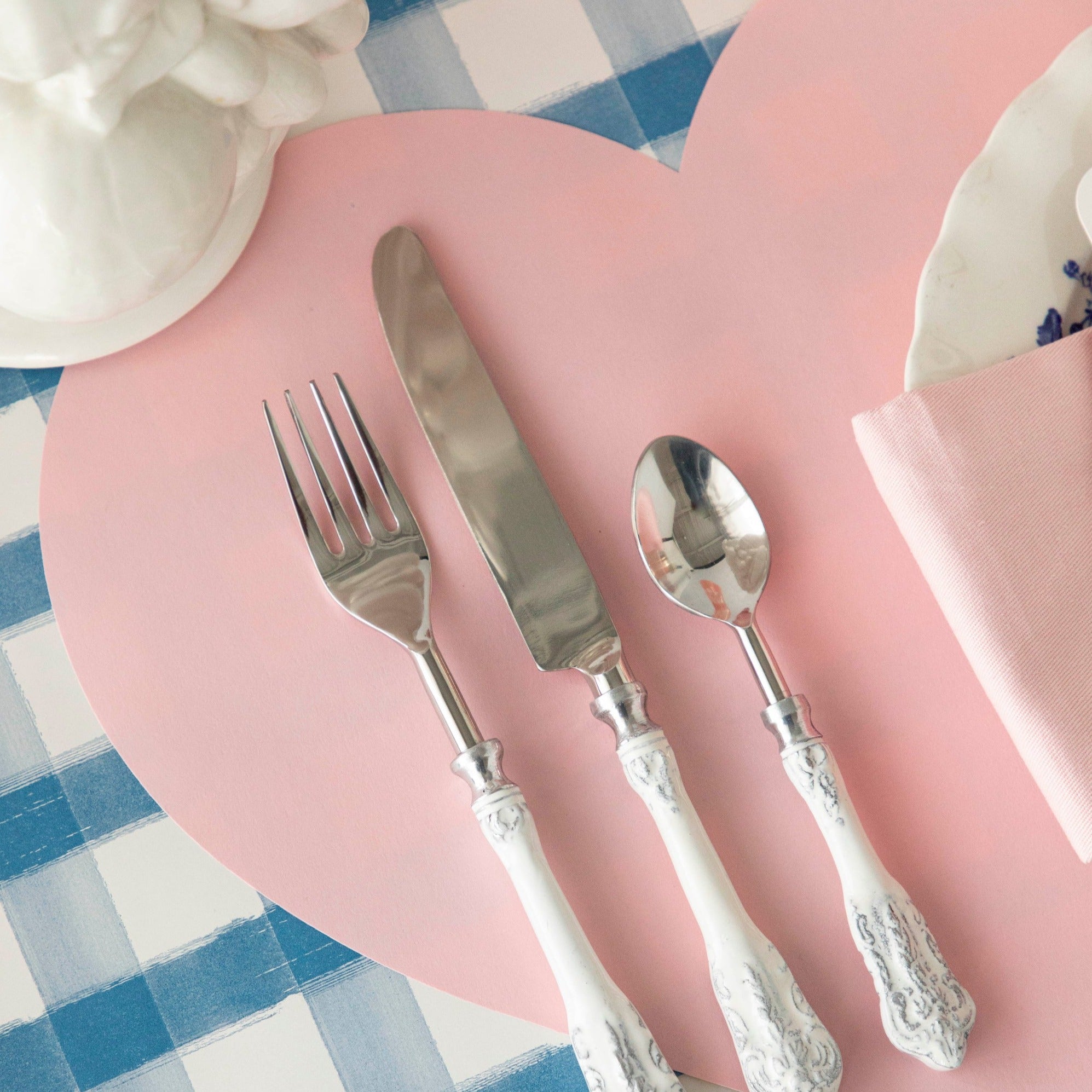 A blue checked tablecloth with silverware and a Die-cut Pink Heart Placemat by Hester & Cook for a Valentine&