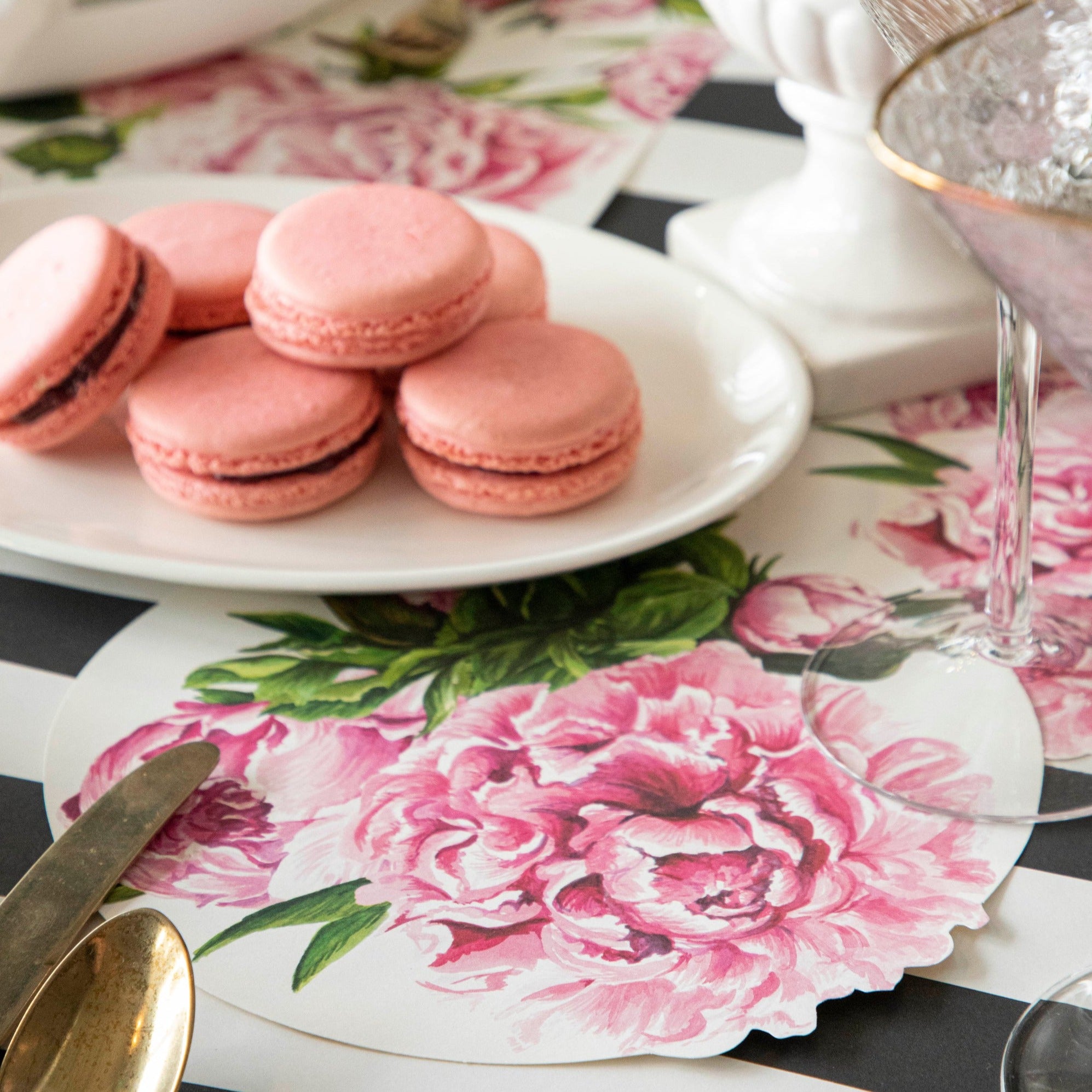 A plate of pink macaroons with a Peony Serving Paper tucked under it on an elegant floral table setting.