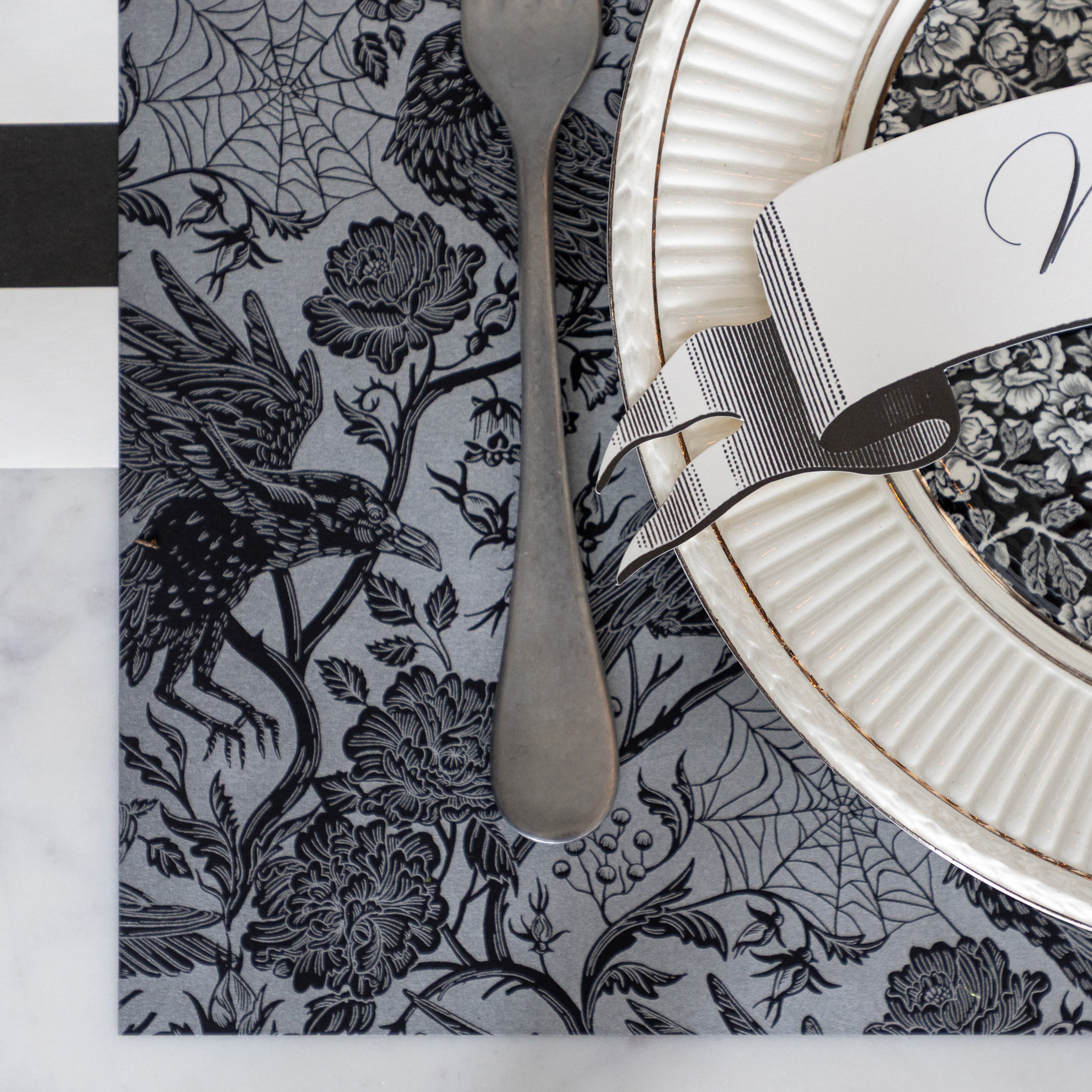 A place setting featuring the Raven Toile Placemat with a silver fork and plates on top and Black Classic Stripe Runner underneath.