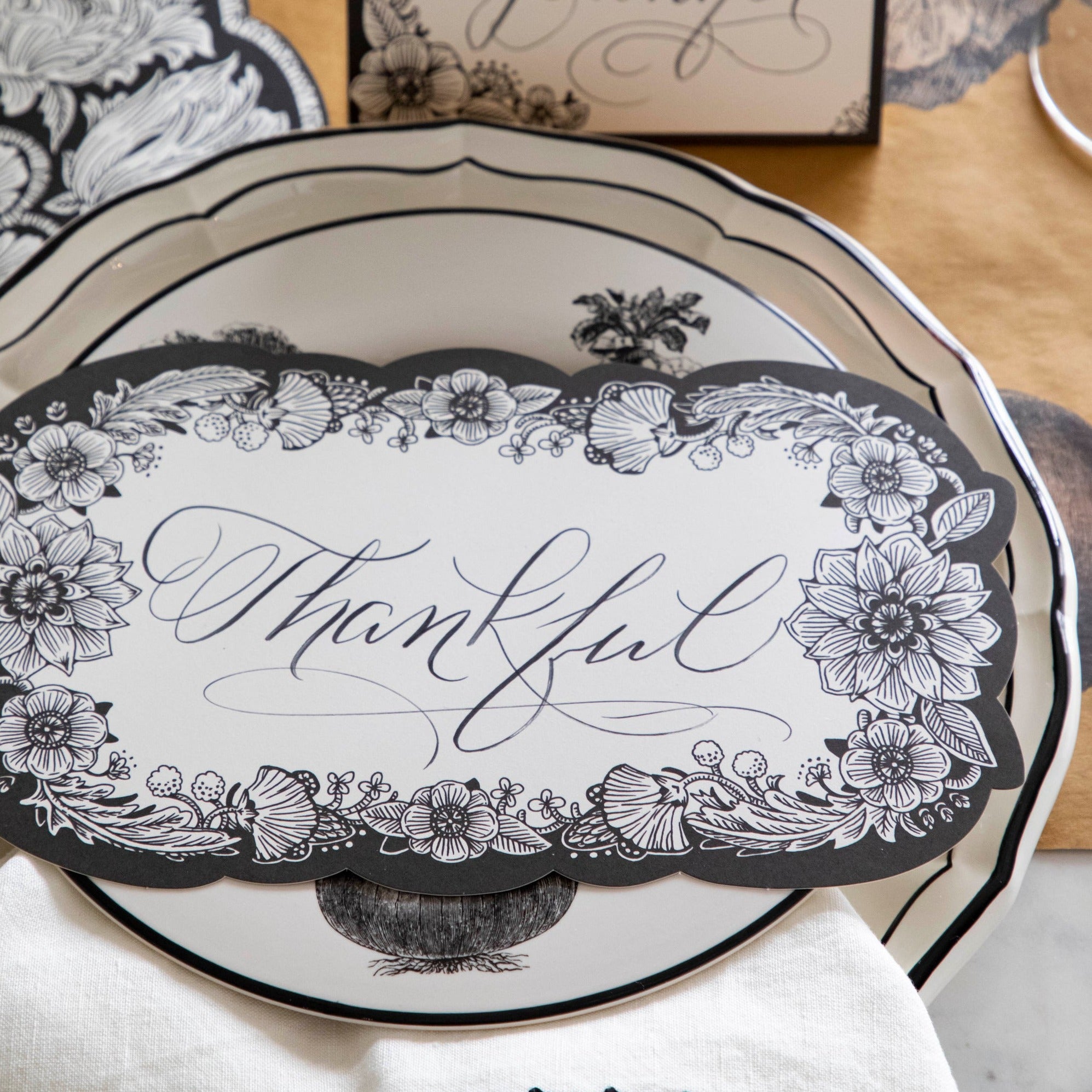 Close-up of an elegant place setting featuring an Ebony Harvest Blooms Table Card with "Thankful" written on it in lovely script resting on the plate.