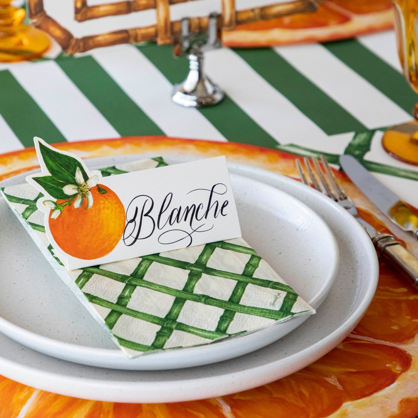 An elegant citrus-themed table setting featuring an Orange Orchard Place Card labeled "Blanche" standing on the Green Lattice Guest Napkin.