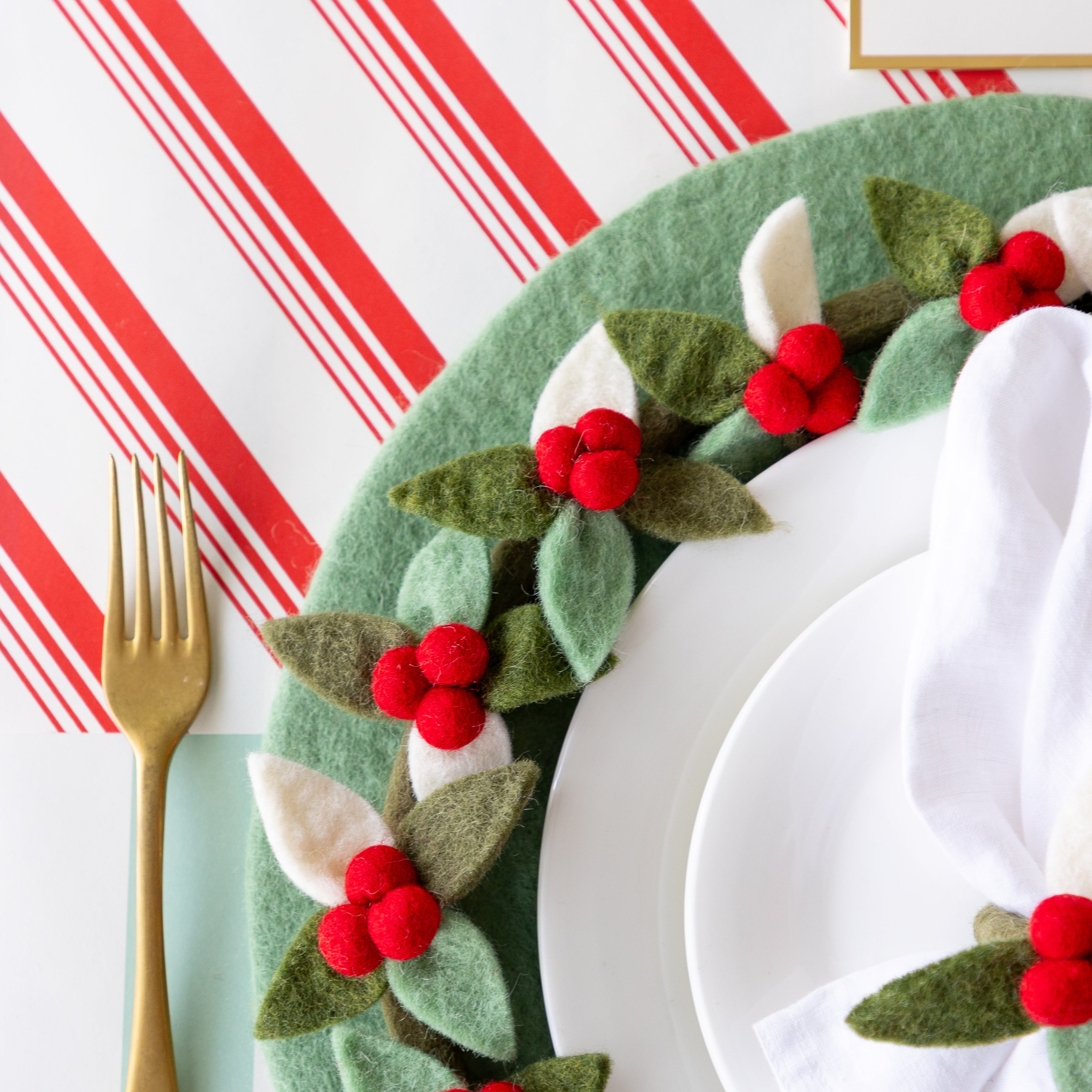 A place setting featuring the Mint Felt Placemat with the Felt Berry Wreath and gold fork atop, and Peppermint Stripe Runner underneath.