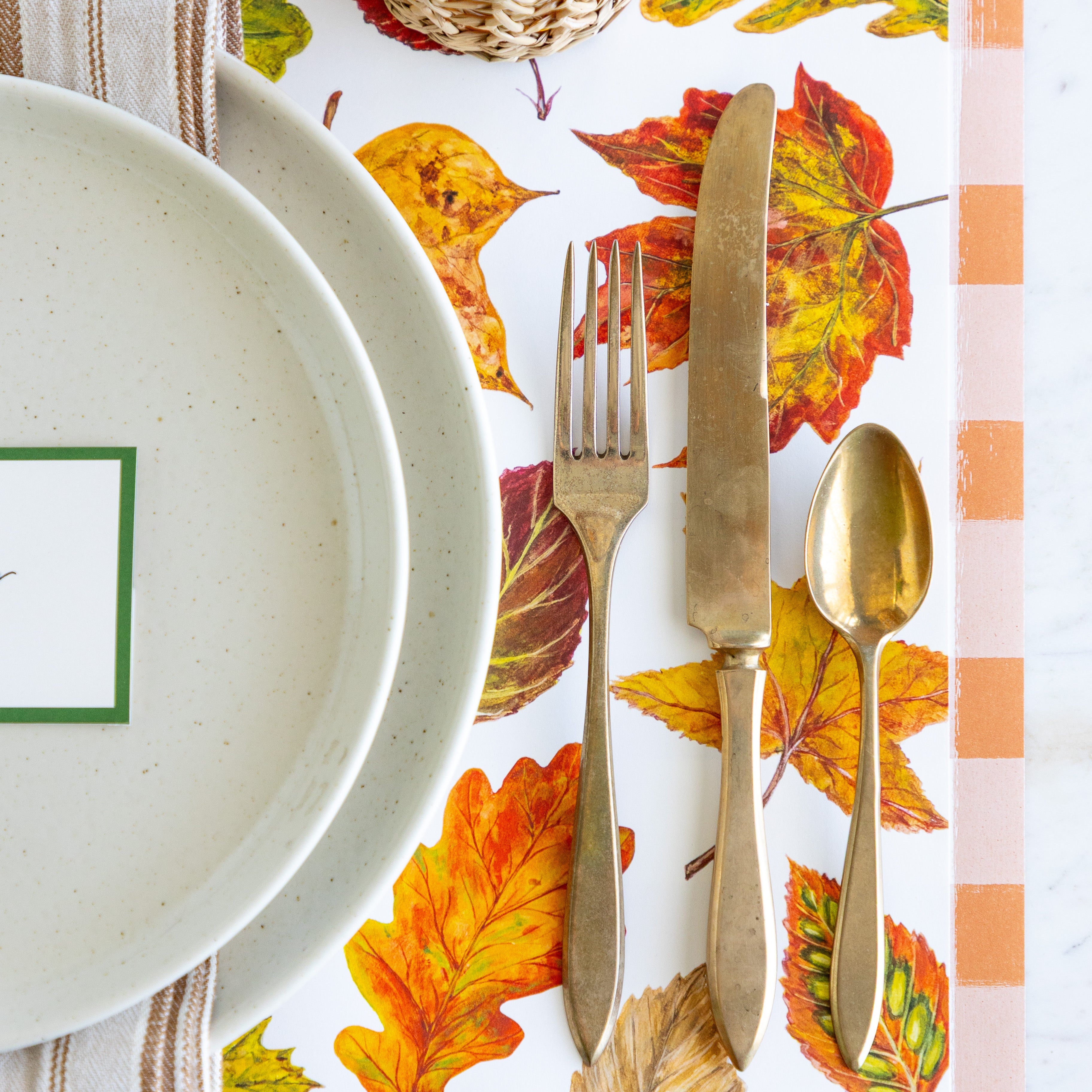 An elegant place setting featuring the Fall Foliage Placemat under Pacifica Salt Dinner Plates, a vintage gold fork, knife and spoon and Orange Painted Check Runner underneath.
