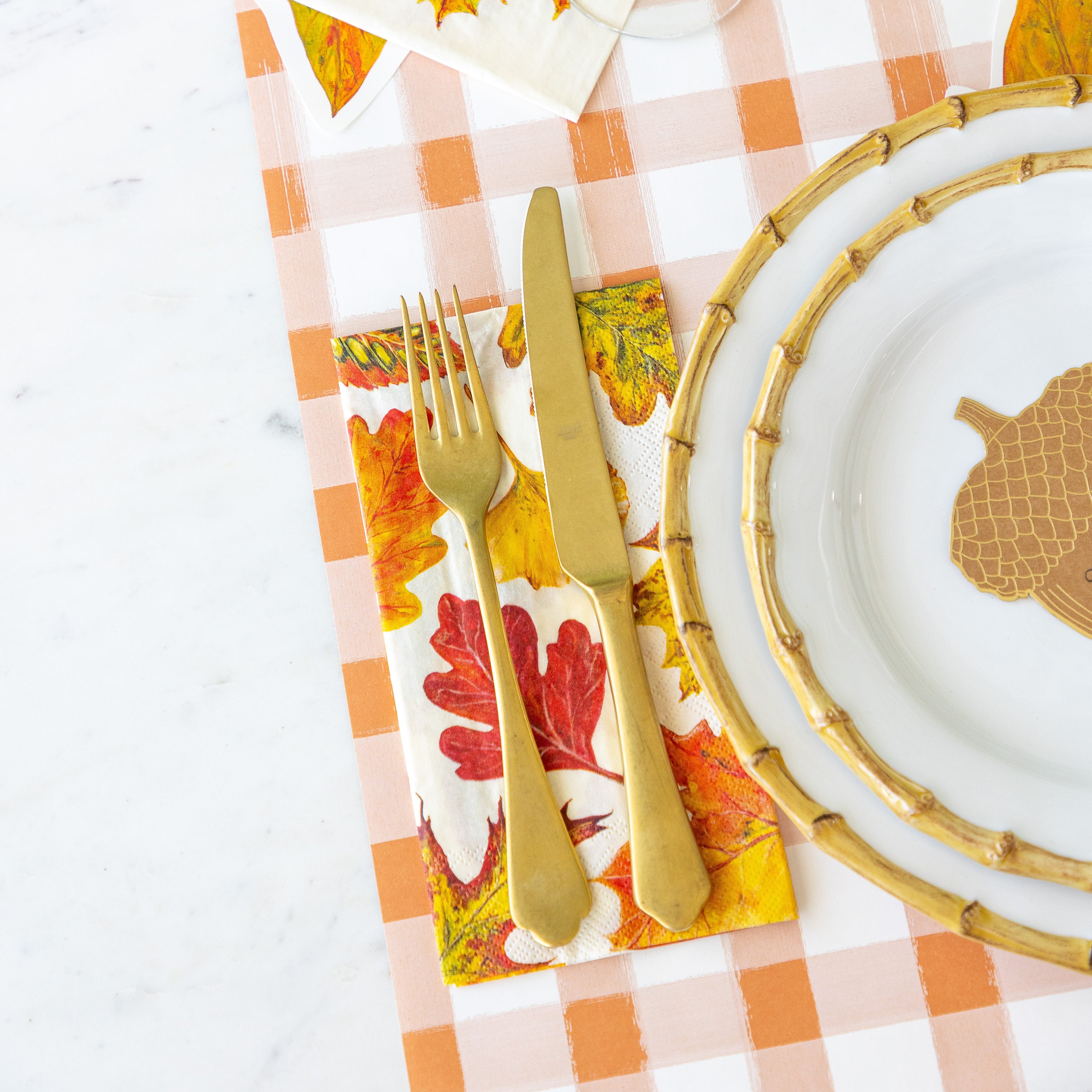 The Fall Foliage Guest Napkin under Mepra Gold fork and knife next to a place setting and the Orange Painted Check Runner underneath.