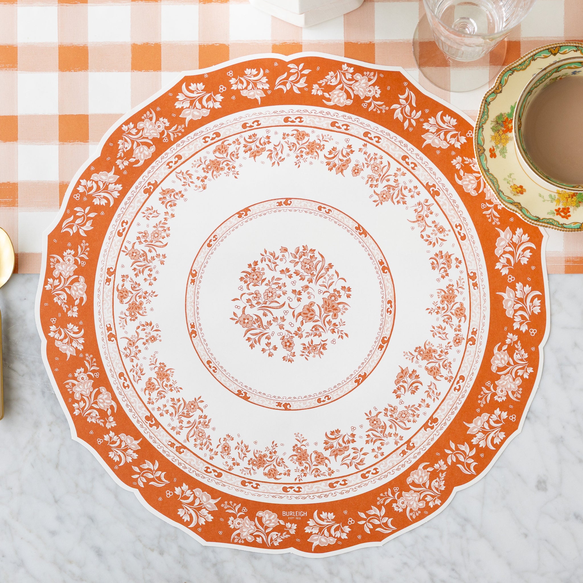 The Die-cut Pumpkin Regal Placemat next to a cup of coffee, on the Orange Painted Check Runner.