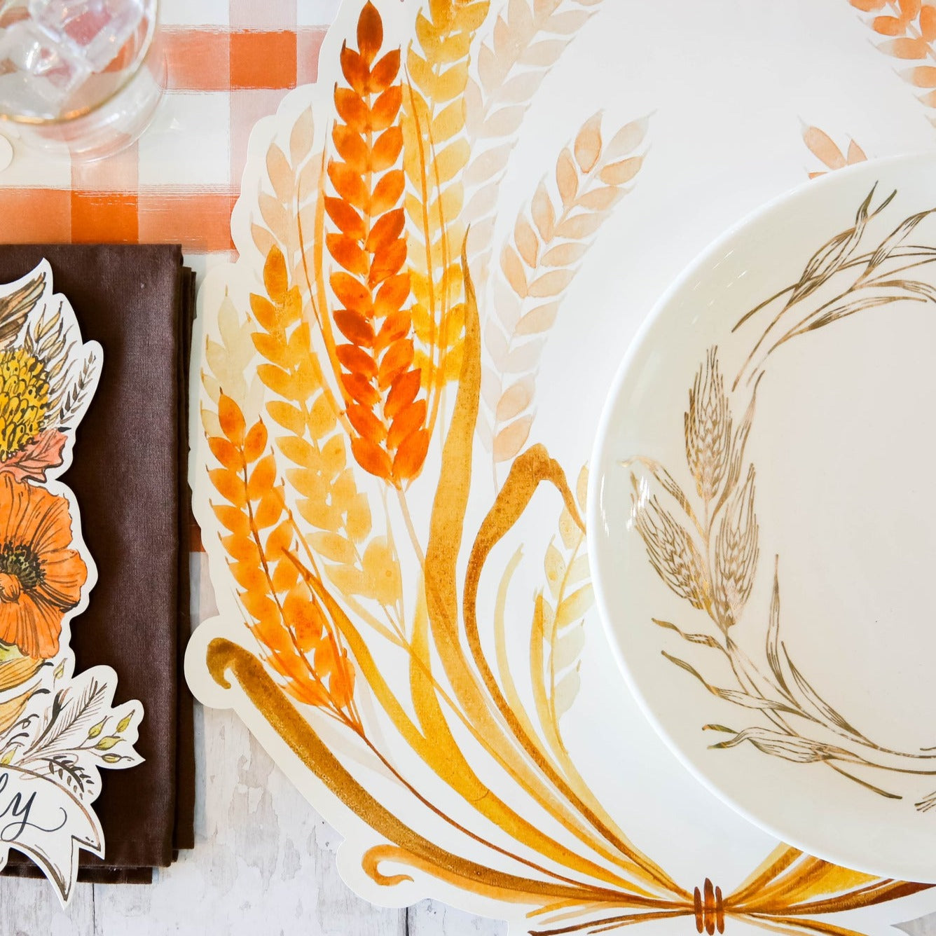 A table setting with a plate, napkin, and Hester & Cook Die-cut Golden Harvest Placemat.