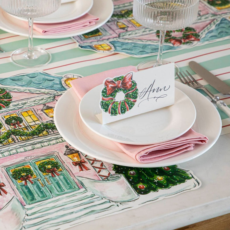 A festive holiday place setting with a Holiday Wreath Place Card labeled &quot;Sara&quot; standing on the plate