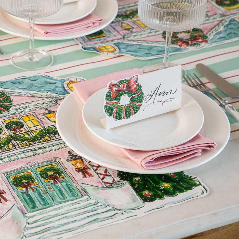 A festive holiday place setting with a Holiday Wreath Place Card labeled "Sara" standing on the plate