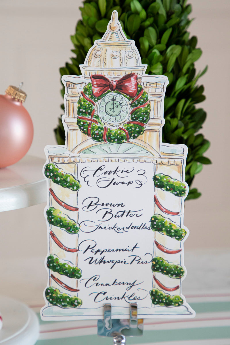A Clock Tower Table Card with a menu written on it in beautiful script standing up in a place card holder on a festive holiday spread.