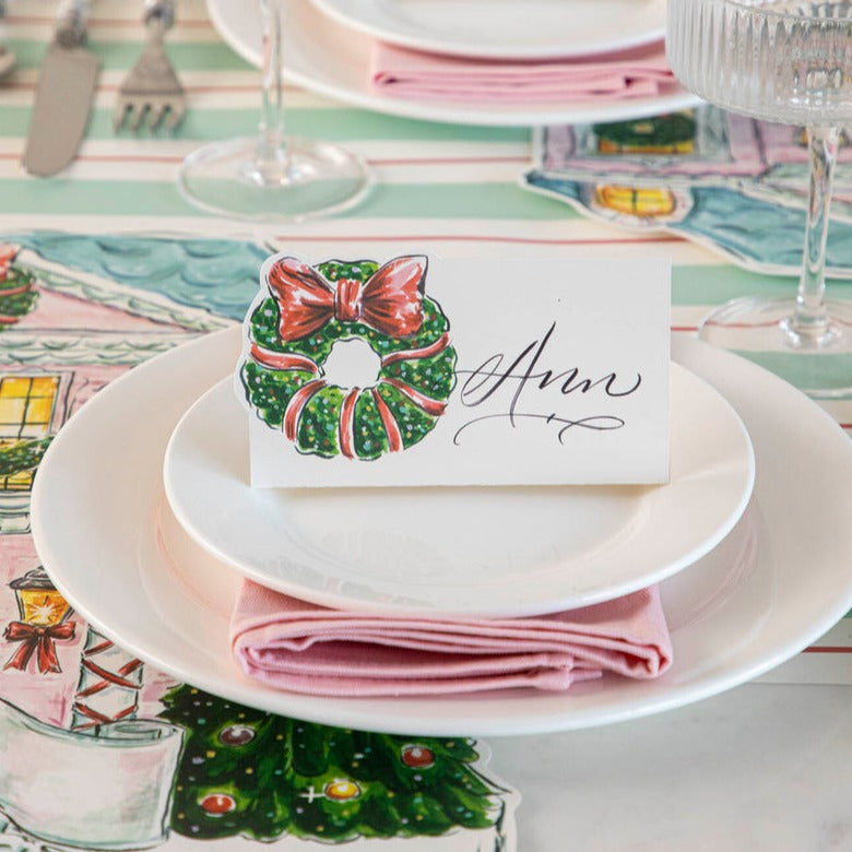 Close-up of an elegant holiday place setting with a Holiday Wreath Place Card labeled &quot;Ann&quot; standing on the plate.