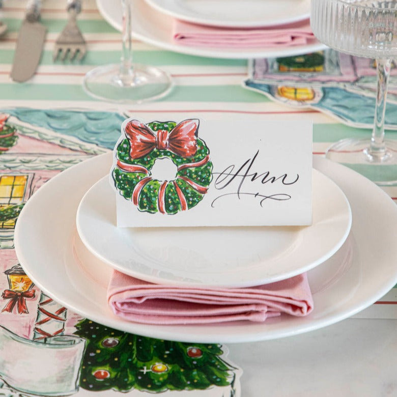 Close-up of an elegant holiday place setting with a Holiday Wreath Place Card labeled "Ann" standing on the plate.