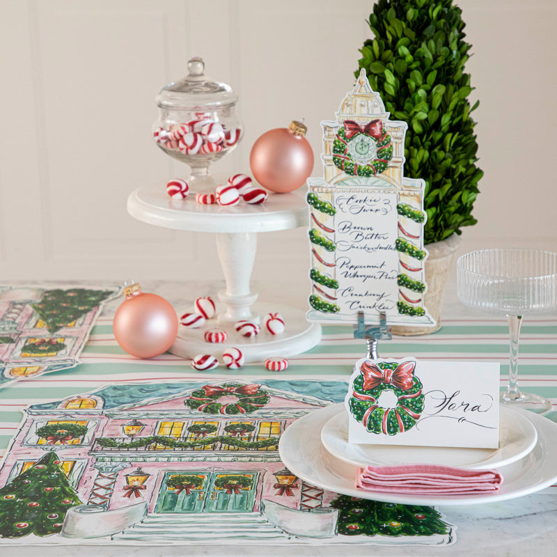 A festive Christmas table setting featuring a Clock Tower Table Card with a menu written on it in beautiful script standing up in a place card holder.