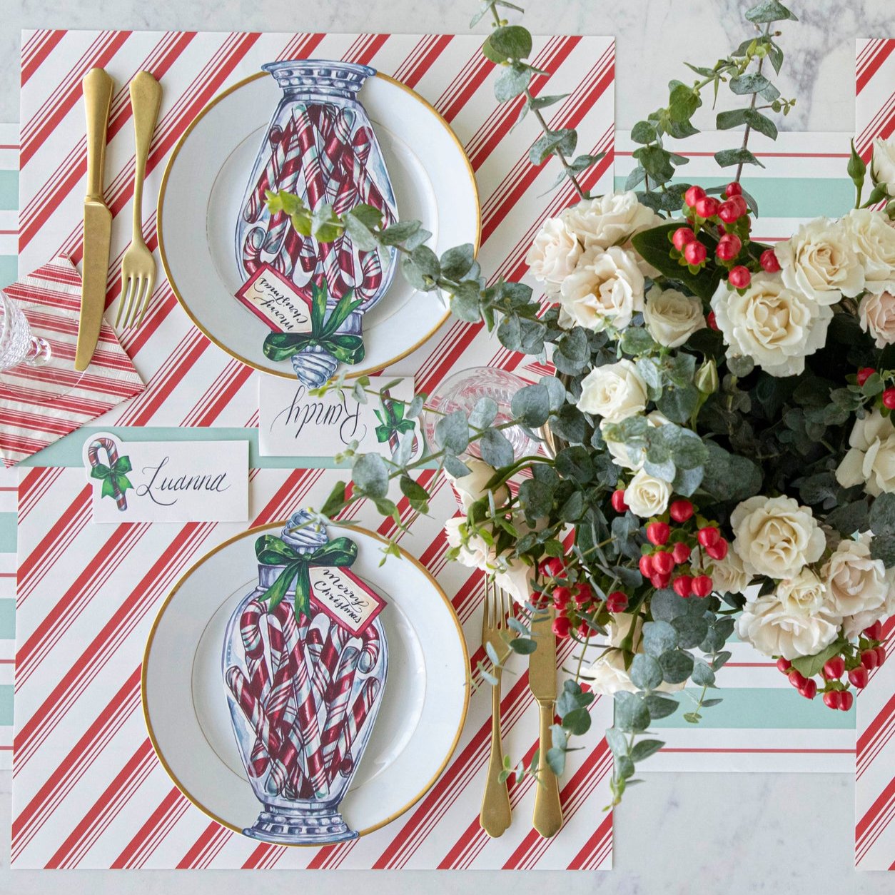 An elegant table setting with a floral arrangement, Peppermint Stripe Placemat on the Seafoam & Gold Awning Stripe Runner, with the Candy Cane Jar Table Accent on a gold rimmed plate.