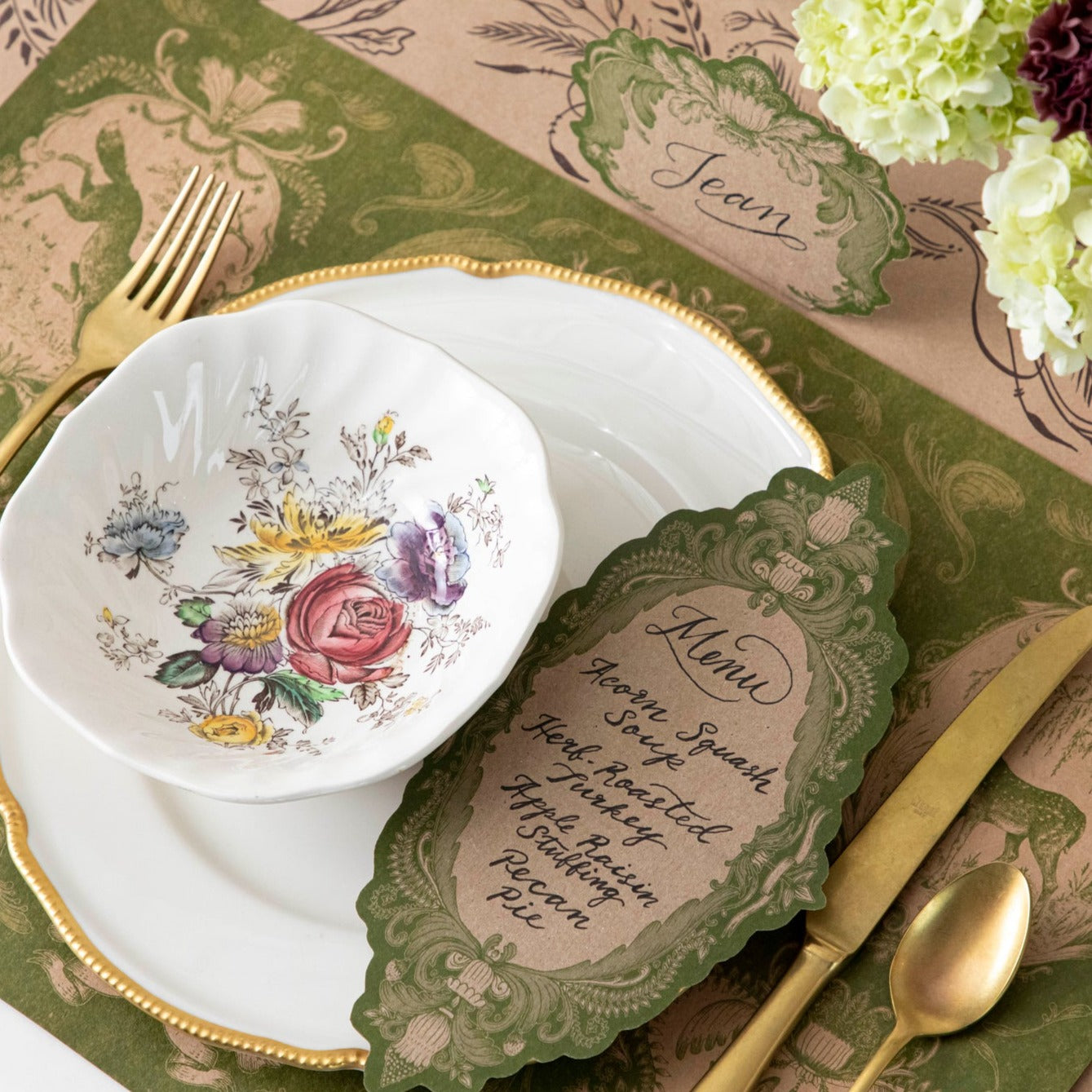 A Moss Fable Toile Table Card with a menu written on it in beautiful script resting on the plate of a rustic place setting.