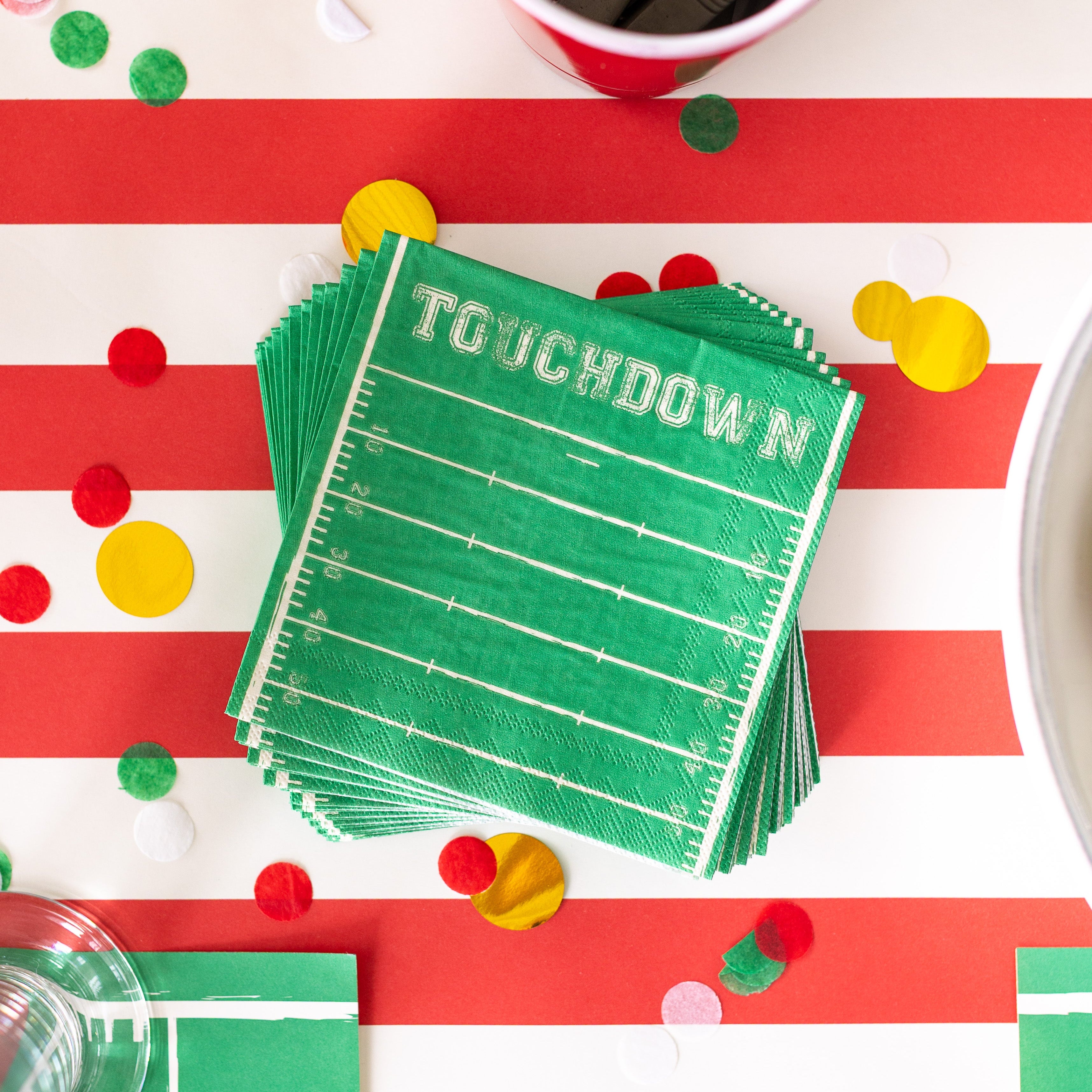 A stack of the Touchdown Cocktail Napkins surrounded by confetti on the Red Classic Stripe Runner.