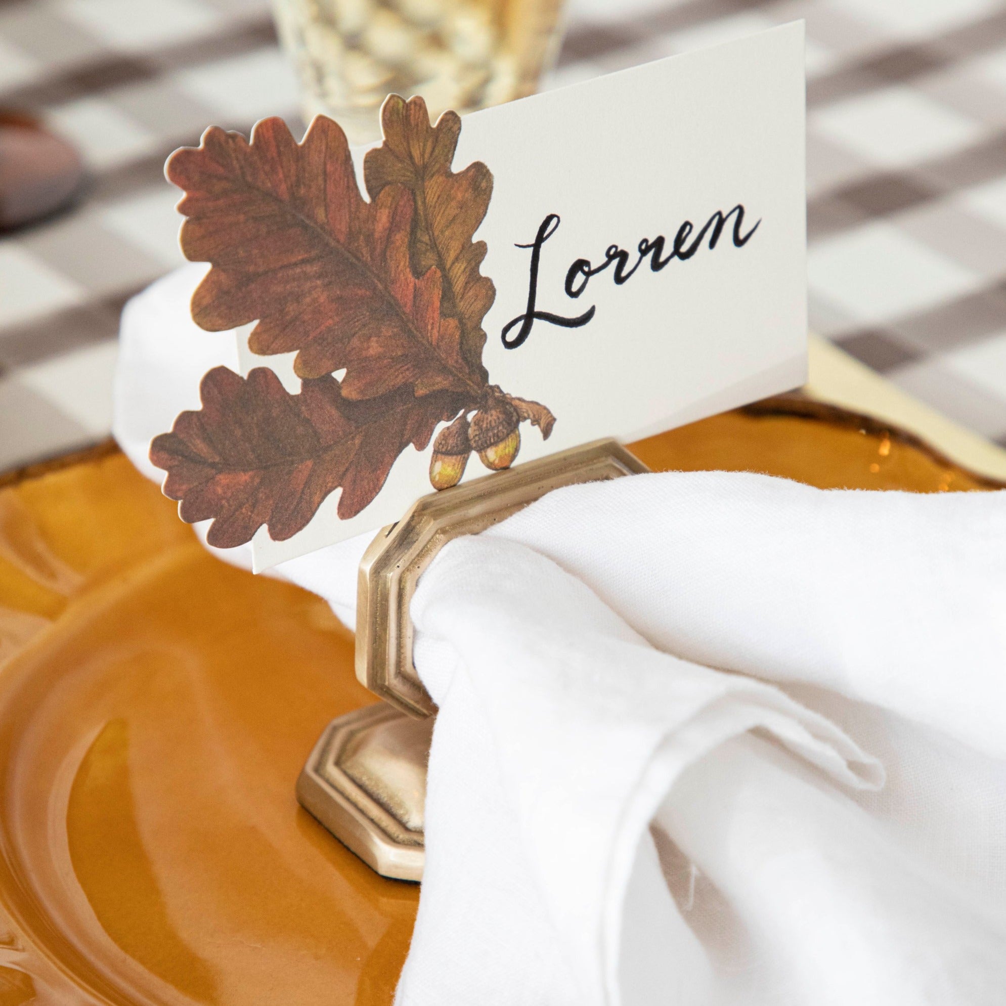 An Autumn Leaves Place Card reading "Lorren" in a napkin ring place card holder on the plate of an elegant place setting.