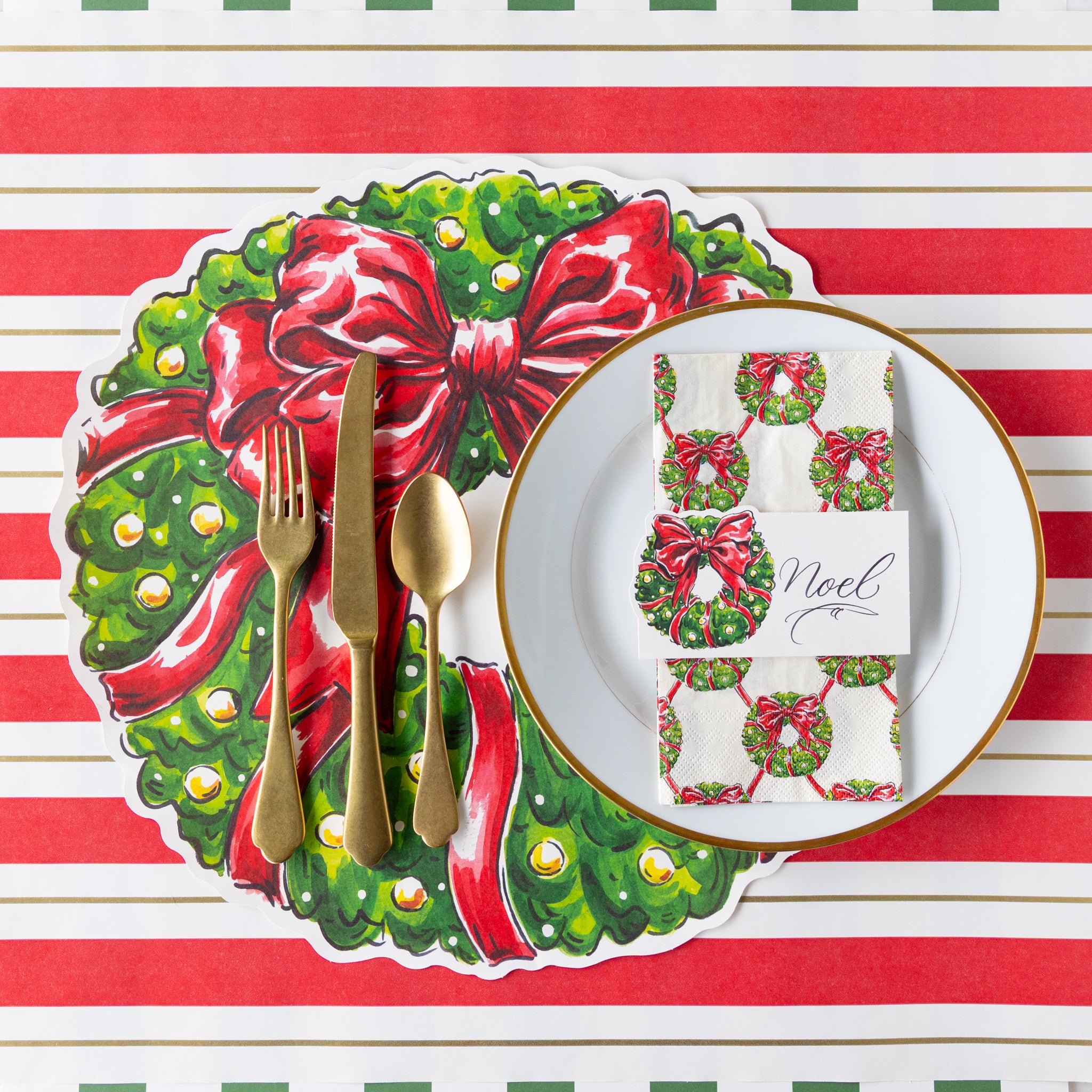 Christmas-themed place setting with decorative plate, cutlery, and napkin on a red and white striped background.