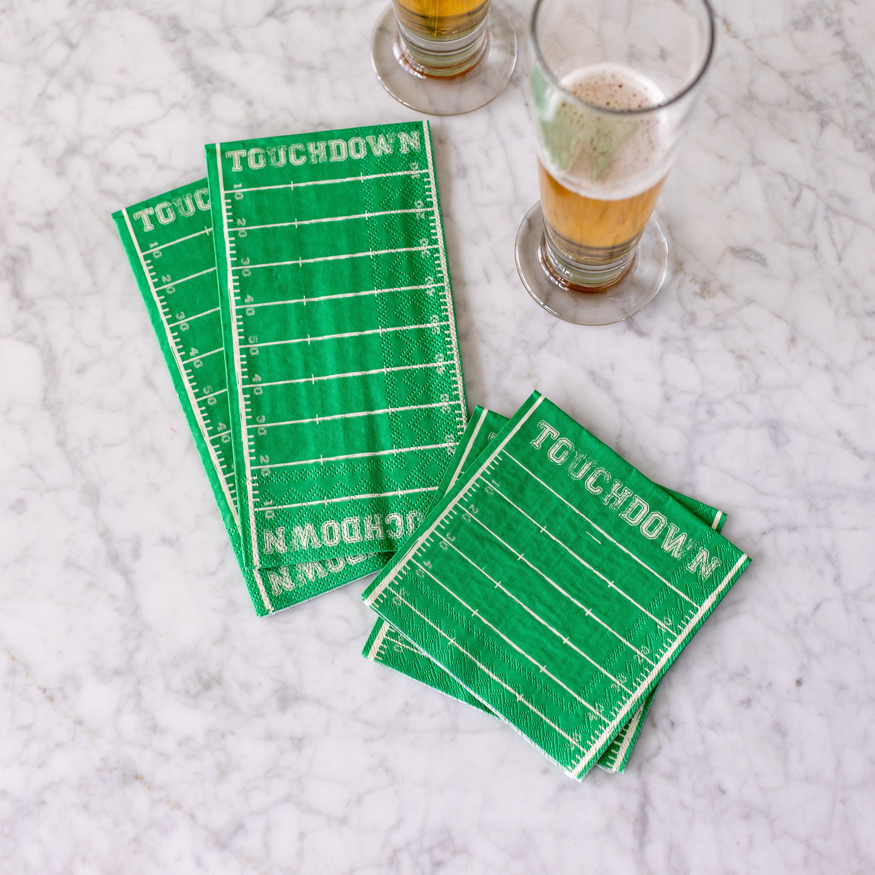 The Touchdown Cocktail and Guest napkins on a table next to glasses of beer.