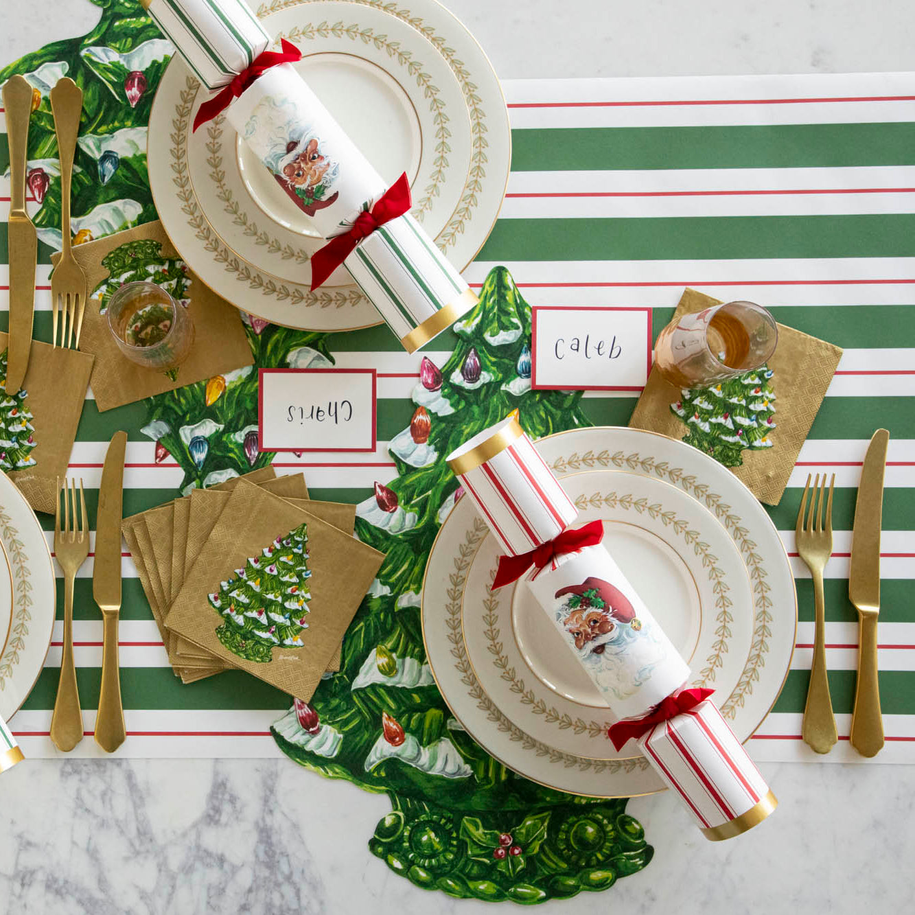 The Green & Red Awning Stripe Runner under a table setting featuring the Die-cut Christmas Tree, elegant plates with the Santa Crackers atop, Red Frame Place Cards, and Christmas Tree Cocktail Napkins.