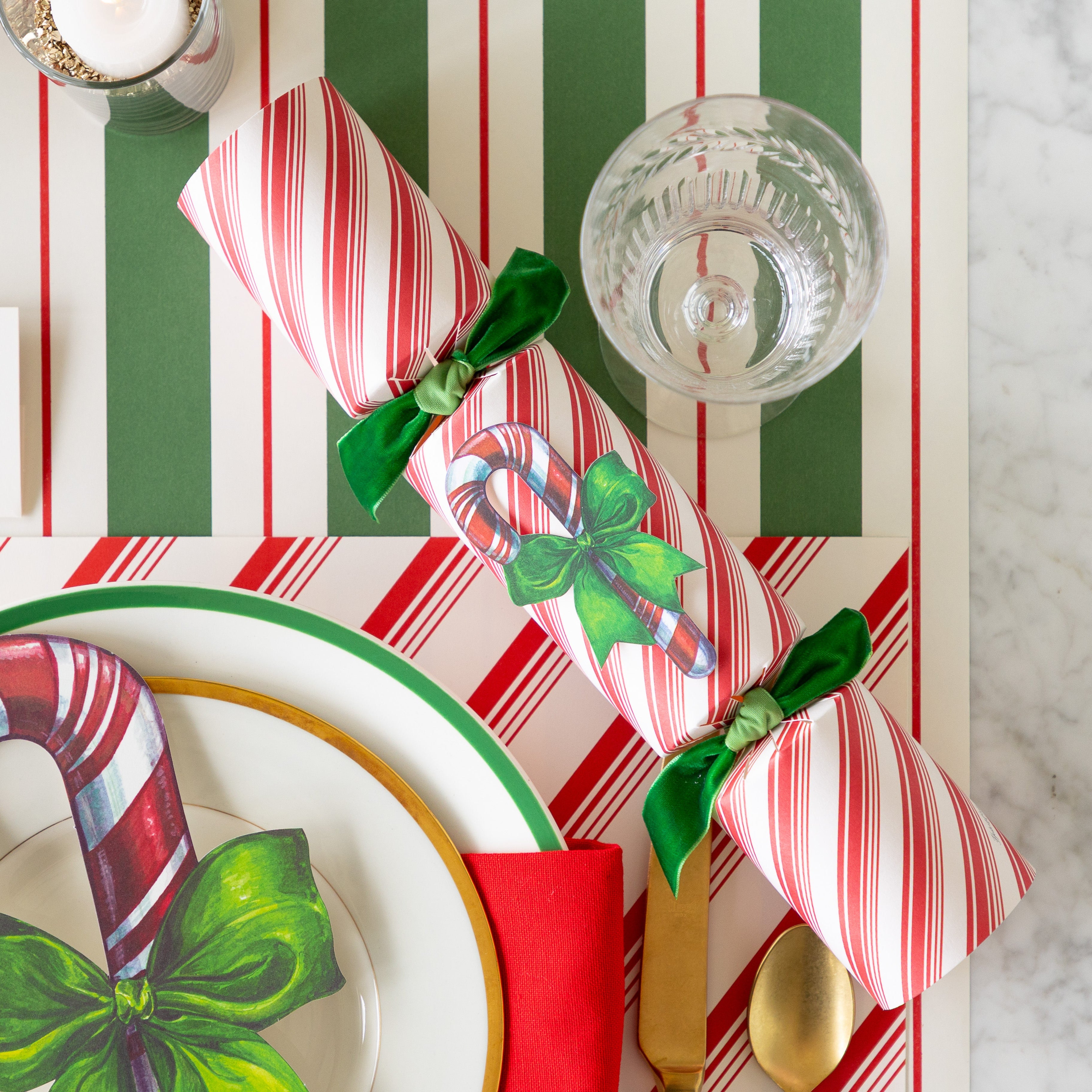 The Candy Cane Cracker next a place setting featuring the Peppermint Stripe Placemat, and Green & Red Awning Stripe Runner underneath.