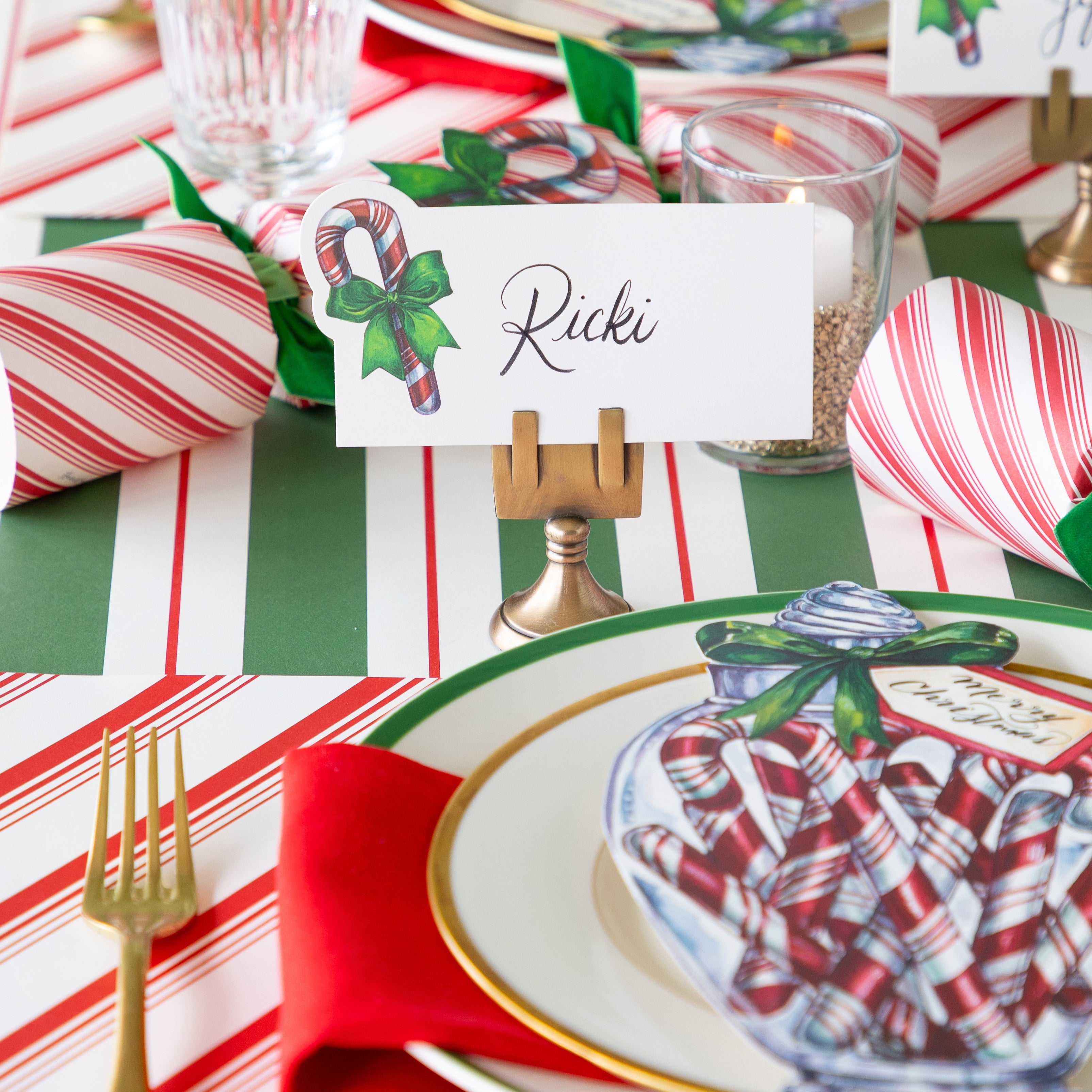 The Candy Cane Place Card reading "Ricki" held by the Brass Place Card Holder, behind a festive place setting.