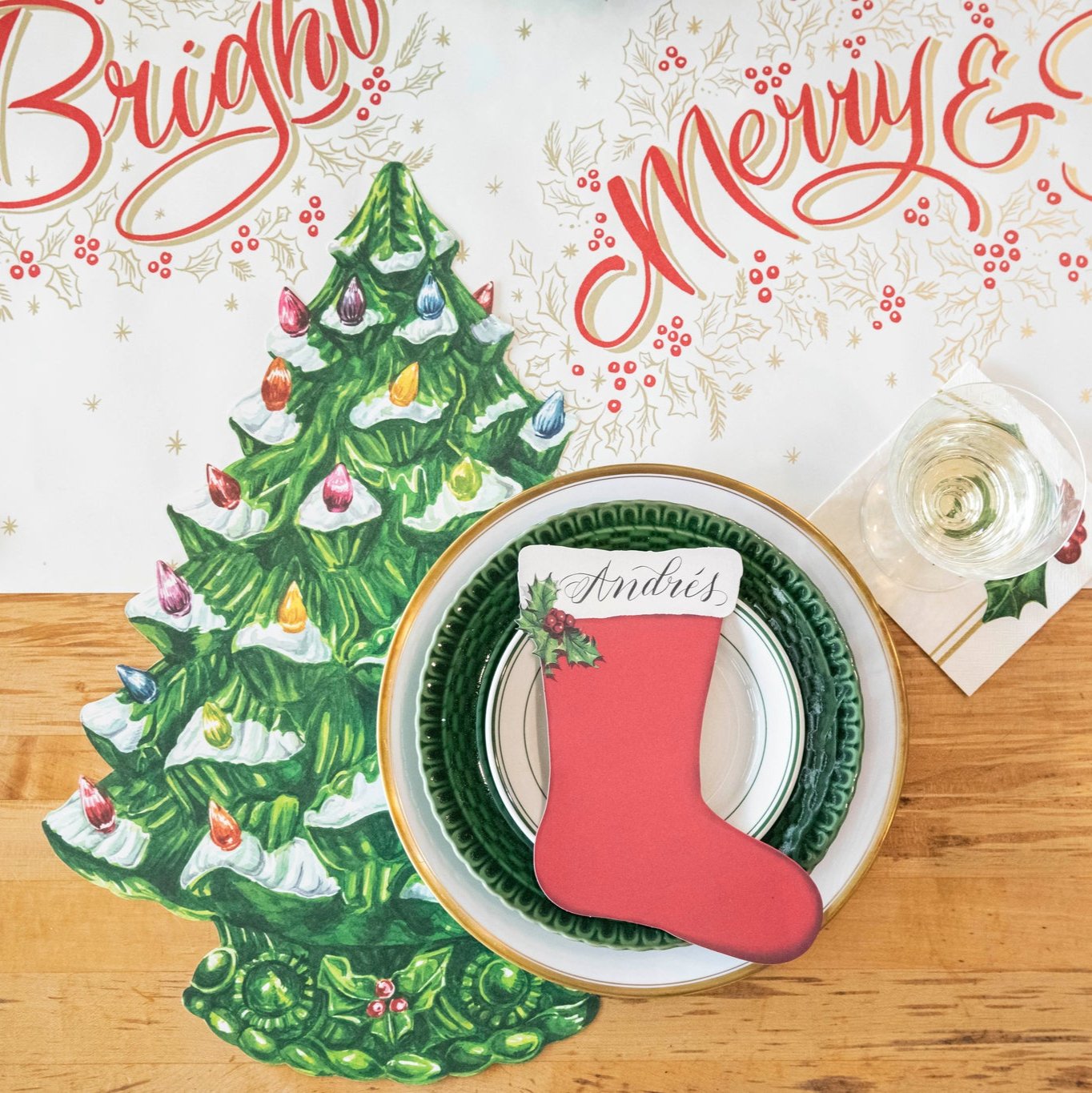 The Stocking Table Accent with "Andres" written on it, resting on a plate, on a Christmas themed table setting.