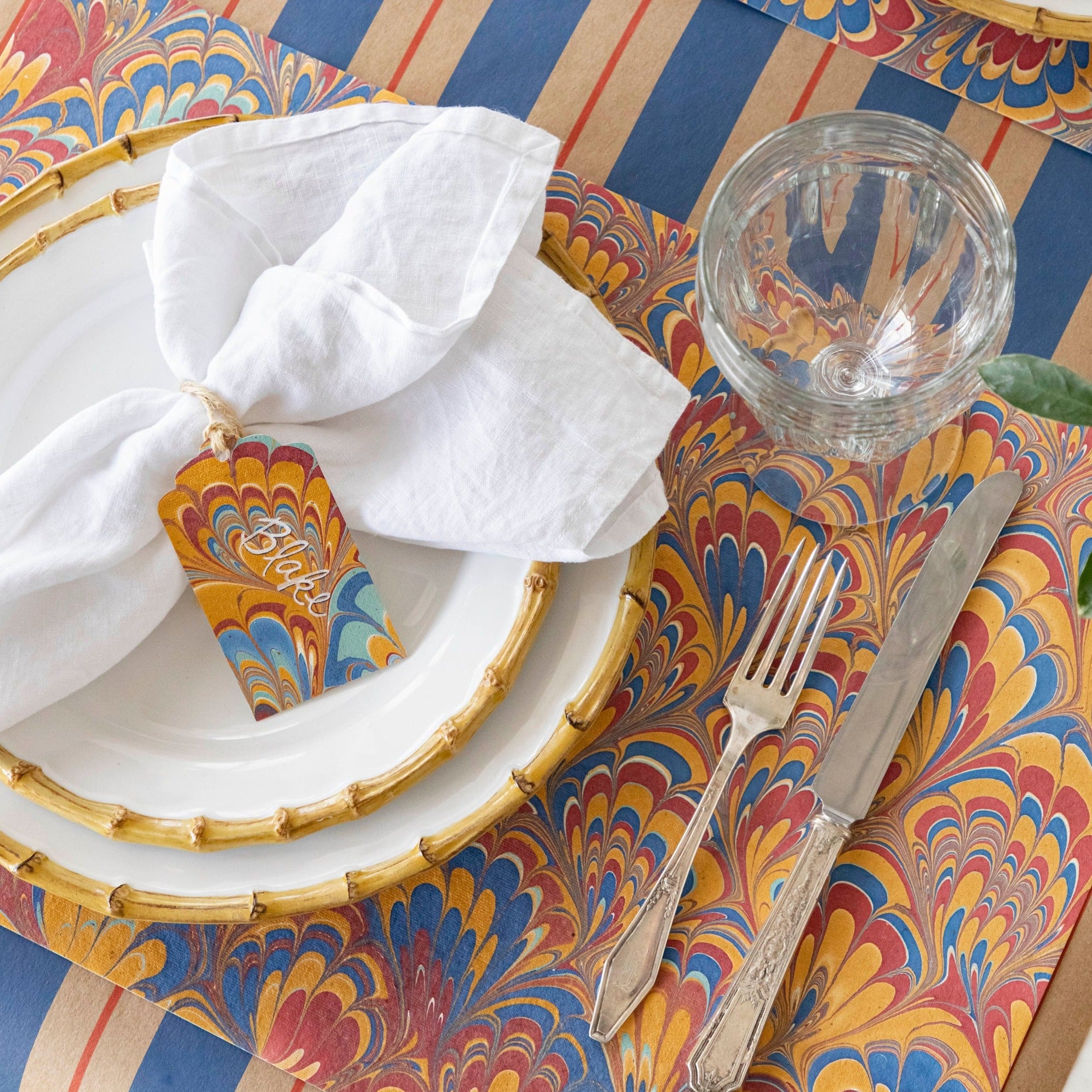 The Red &amp; Blue Peacock Marbled Placemat under an elegant place setting.