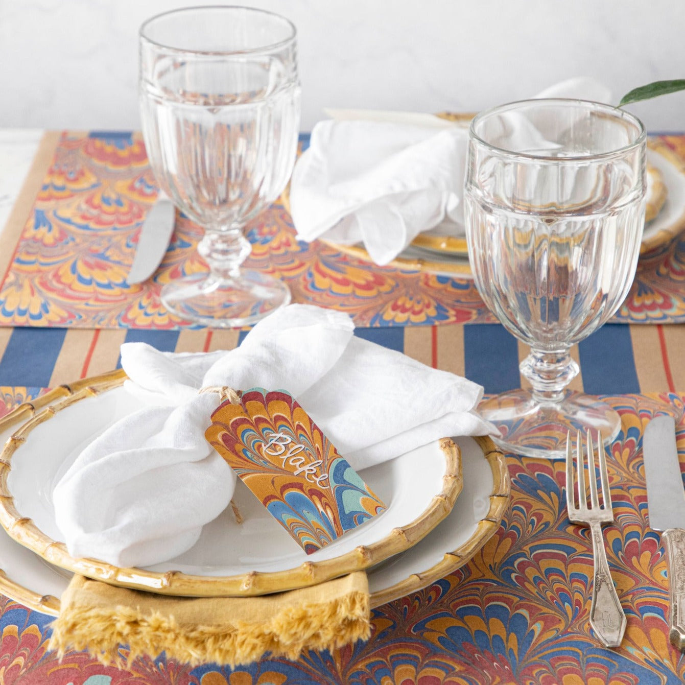 The Red &amp; Blue Peacock Marbled Placemat under an elegant table setting for two.