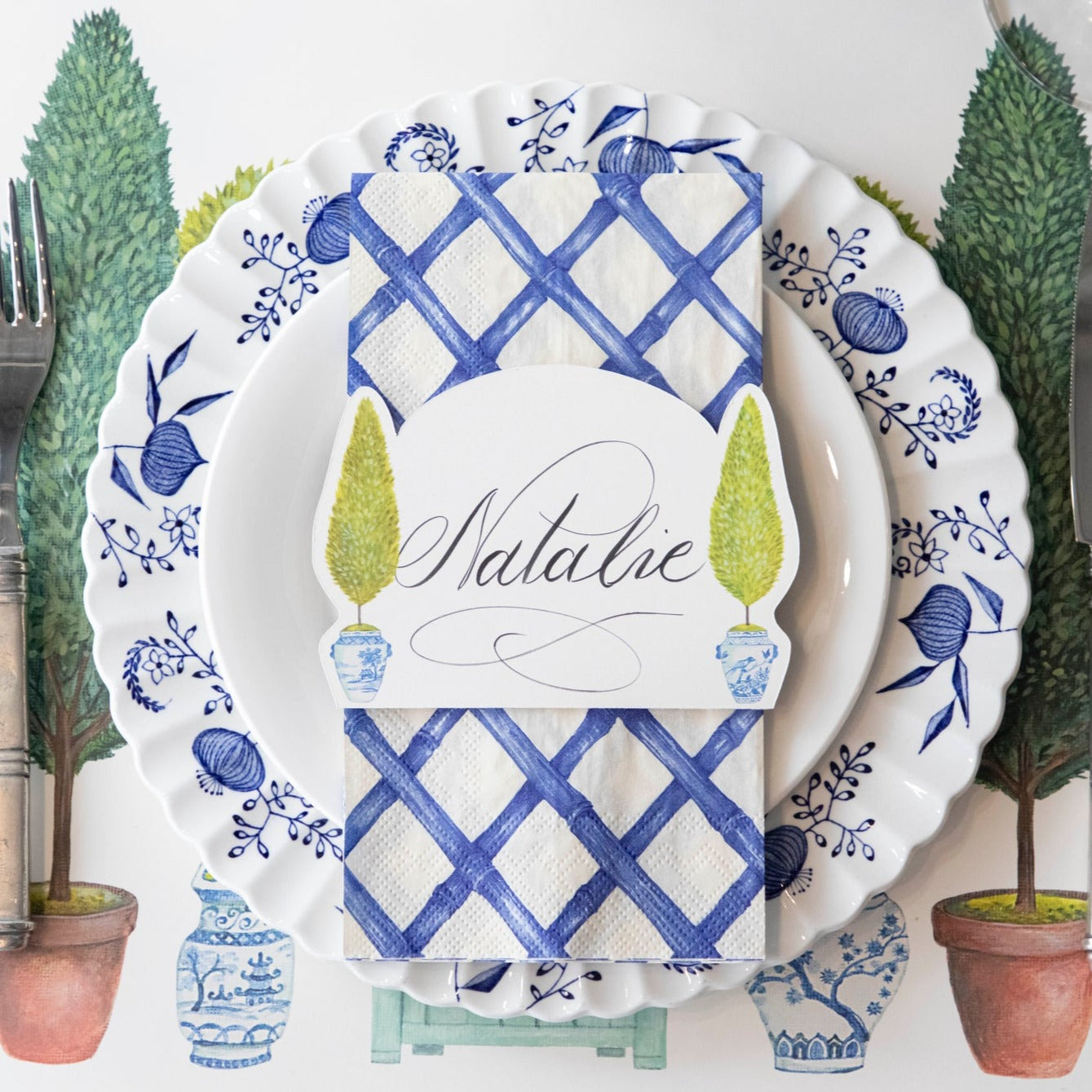 Top-down view of an elegant place setting featuring a Topiary Place Card labeled "Natalie" laying flat on the plate.