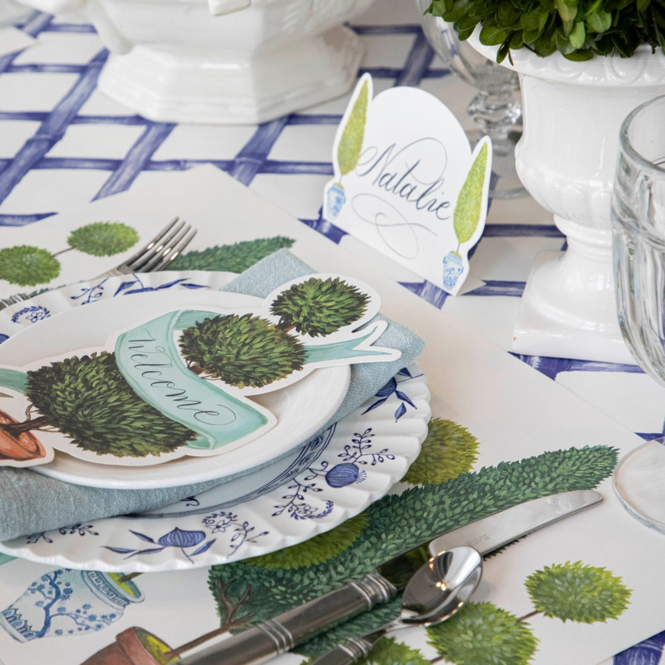 Close-up of the Topiary Garden Placemat in an elegant place setting, showing the illustrated foliage in detail.