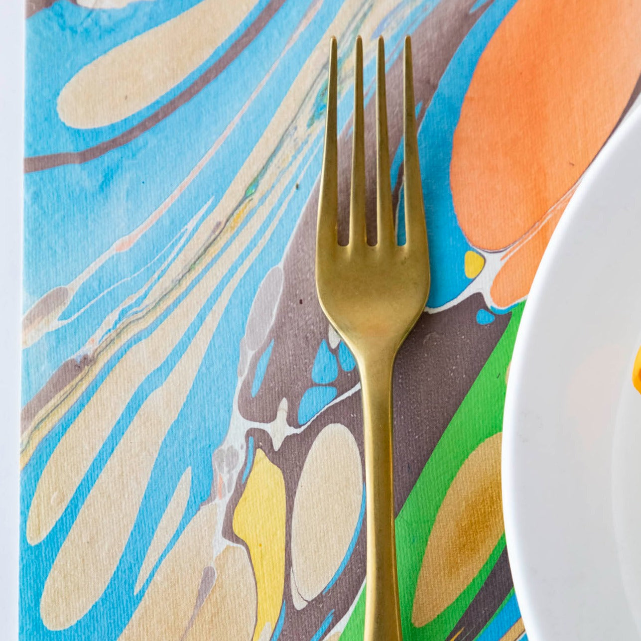 Close-up of a gold fork on the Multi Color Fantasy Marbled Placemat, showing a vibrant swish of color.