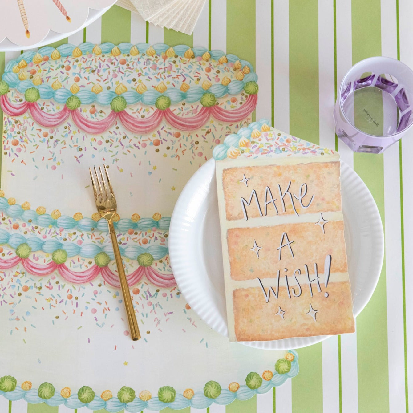 A vibrant birthday party place setting featuring a Cake Slice Table Accent resting on the plate with "Make A Wish!" written in white ink with a black outline.