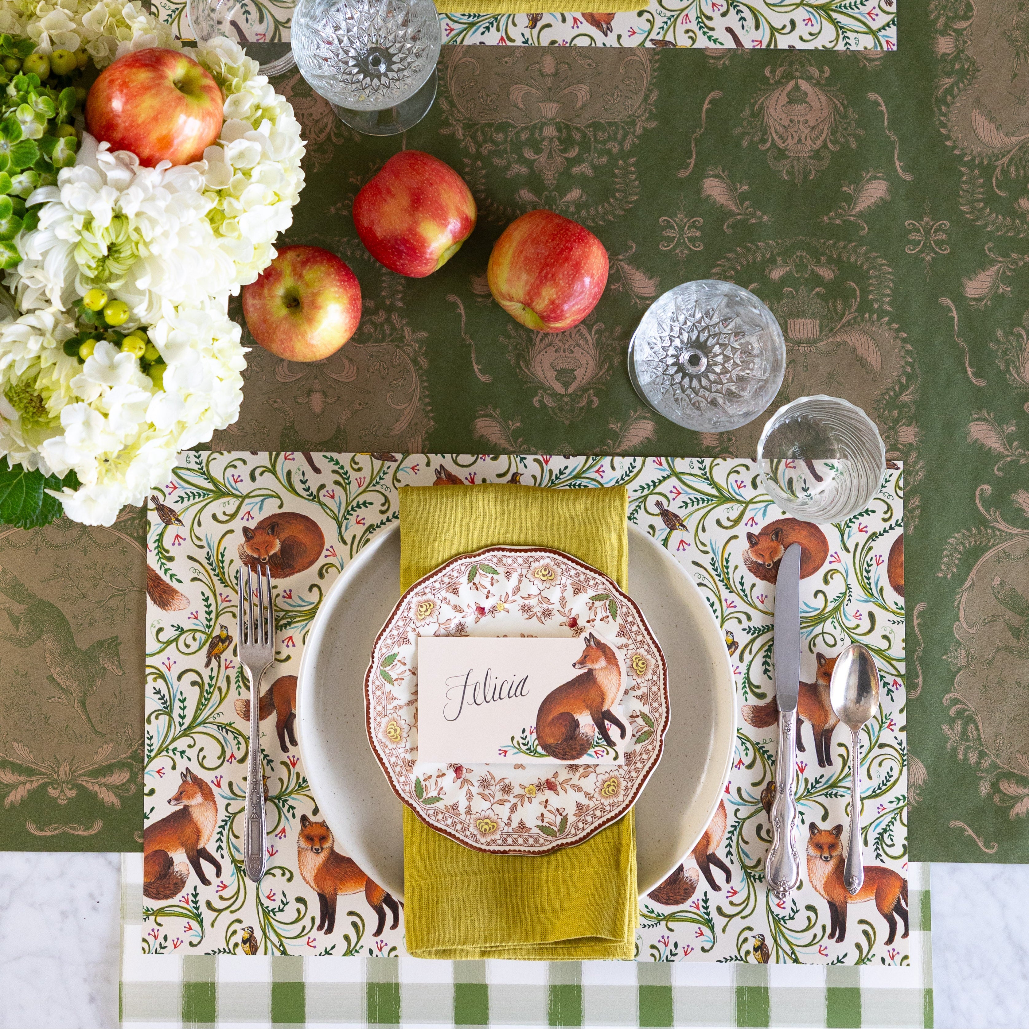 Fanciful Foxes Placemat on an elegant table setting with vintage dinnerware and silverware, Fanciful Fox Place Card with "Felicia" written on it, Moss Fable Toile Runner horizontally on the table and Moss Green Painted Check Runner vertically under the place setting.
